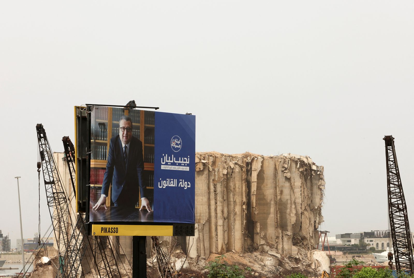 لوحة إعلانية تُروج لأحد المرشحين للانتخابات النيابية اللبنانية وفي الخلفية أطلال مرفأ بيروت الذي انفجر عام قبل نحو عامين- 18 أبريل 2022 - REUTERS