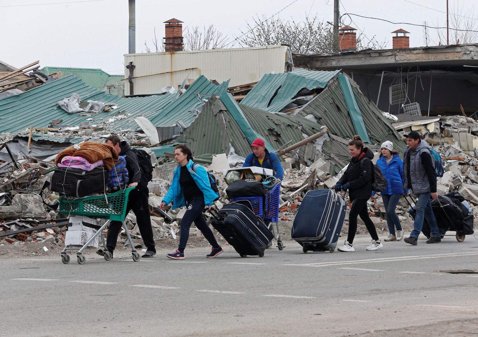 أوكرانيون يجرون حقائبهم أمام أطلال مبانيهم المدمرة في ماريوبل. 19 أبريل 2022 - REUTERS