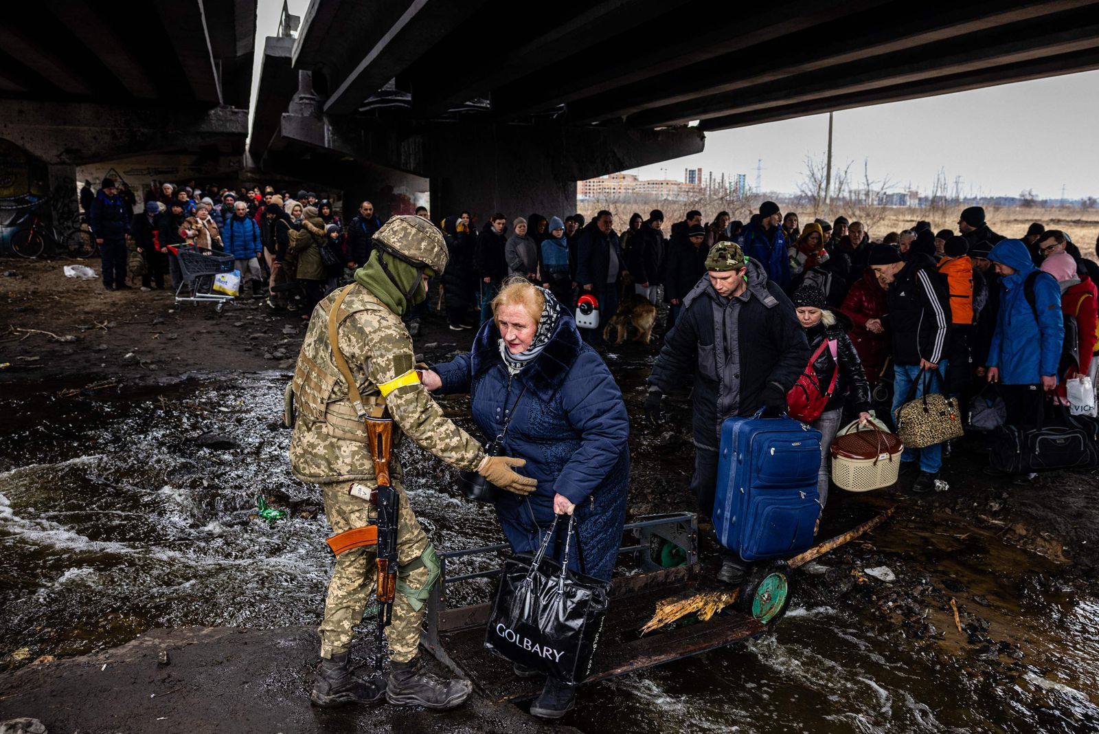 A Ukrainian serviceman helps evacuees gathered under a destroyed bridge, as they flee the city of Irpin, northwest of Kyiv, on March 7, 2022. - Ukraine dismissed Moscow's offer to set up humanitarian corridors from several bombarded cities on March 7, 2022, after it emerged some routes would lead refugees into Russia or Belarus. The Russian proposal of safe passage from Kharkiv, Kyiv, Mariupol and Sumy had come after terrified Ukrainian civilians came under fire in previous ceasefire attempts. (Photo by Dimitar DILKOFF / AFP) - AFP