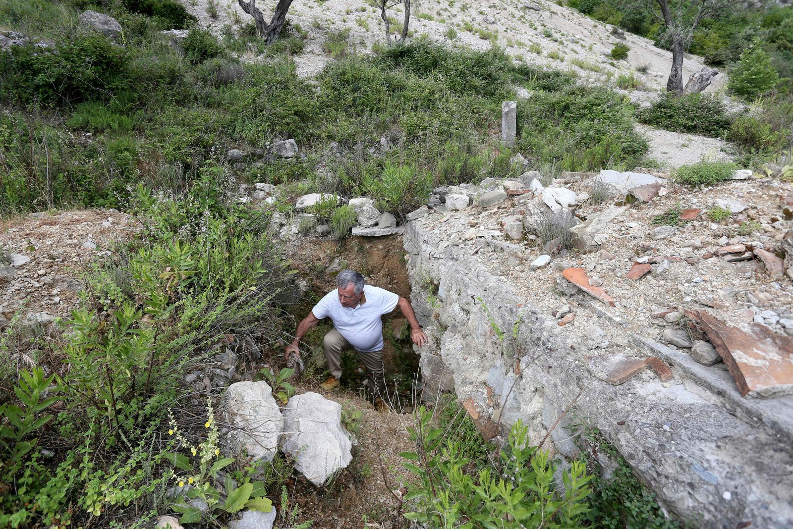 Archaeologist, Skender Mucaj inspects holes dug by illegal treasure hunters at the ruins of the Church of St. Mary in Brrar, near the city of Tirana on June 13, 2022. The Church of St. Mary is an archeological site of an 11th-century monument that has been heavily damaged by illegal digs. - In an ancient Albanian city abandoned to its fate, treasure looters dig holes in search of gold, silver or rare archaeological pieces that they could resell. (Photo by Gent SHKULLAKU / AFP) - AFP