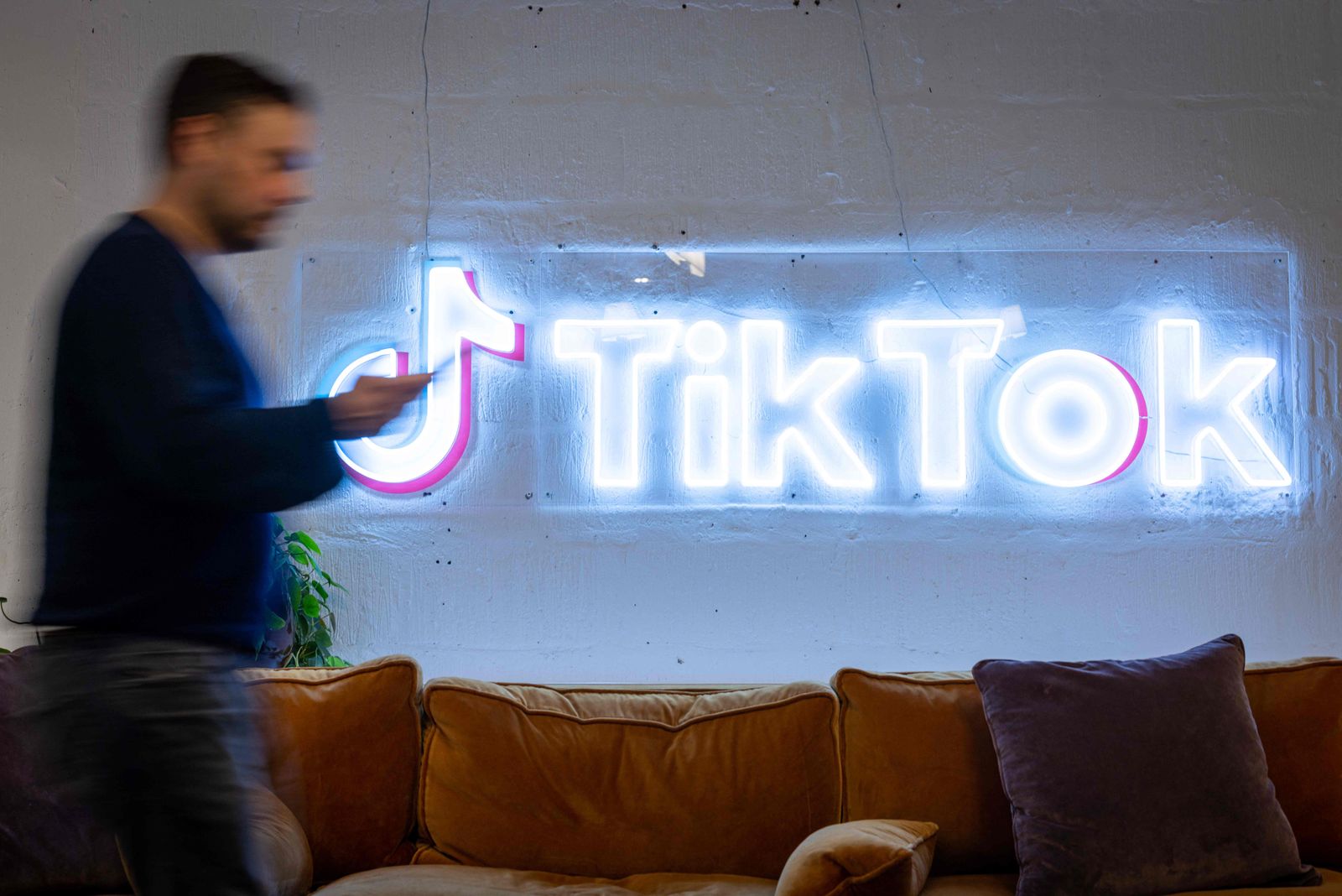 (FILES) In this file photo taken on February 09, 2022 an employee looks at his mobile phone as he walks past the logo of the video-focused social networking service TikTok, at the TikTok UK offices, in London. - TikTok on August 17, 2022 rolled out its battle plan against the deluge of misinformation expected to accompany the upcoming US midterm elections, a problem tech firms largely decide themselves how to handle. (Photo by Tolga Akmen / AFP) - AFP