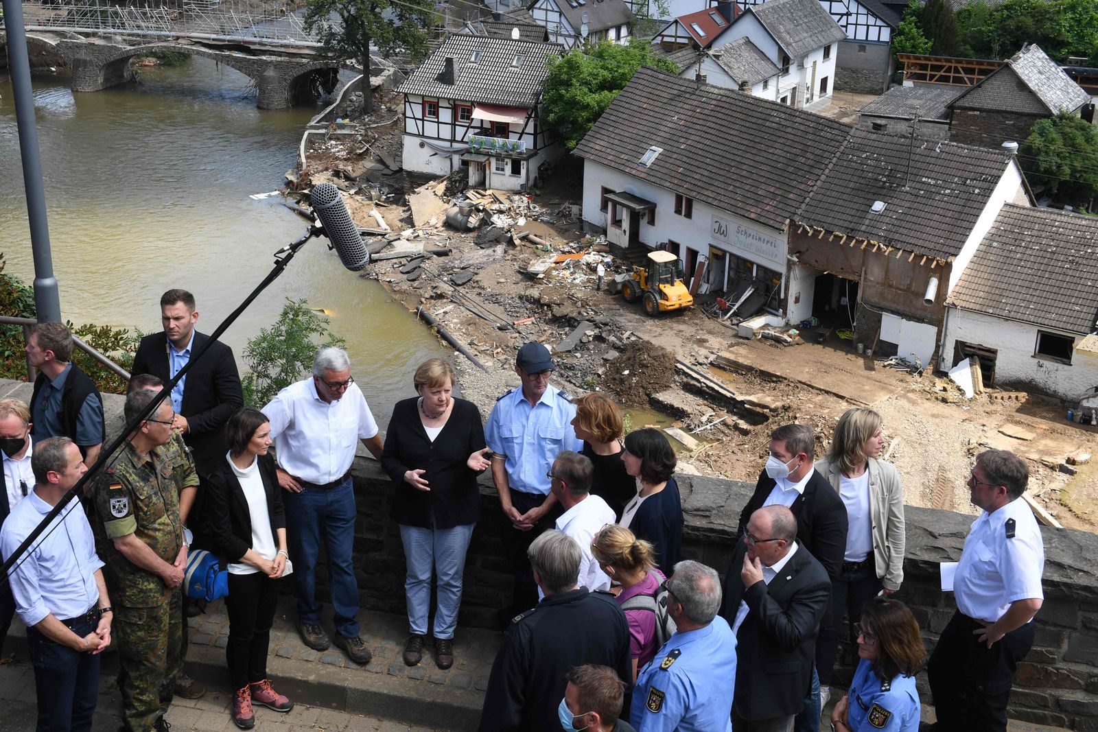 German Chancellor Angela Merkel (C-L) and Rhineland-Palatinate State Premier Malu Dreyer (C-R) speak to people as they stand a bridge during their visit in the flood-ravaged areas, in Schuld near Bad Neuenahr-Ahrweiler, Rhineland-Palatinate state, western Germany, on July 18, 2021. - After days of extreme downpours causing devastating floods in Germany and other parts of western Europe which have been described as a 