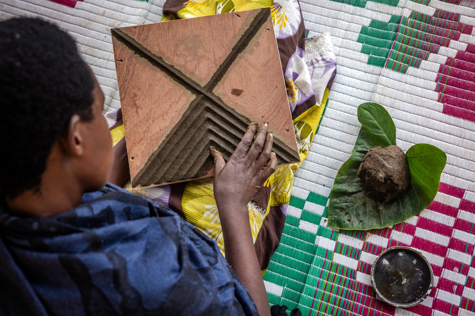 أحد الناجين من الإبادة الجماعية يرسم أنماطاً من فن إيميجونجو التقليدي على لوح خشبي باستخدام روث البقر في كيريهي برواندا. 4 أبريل 2024 - AFP