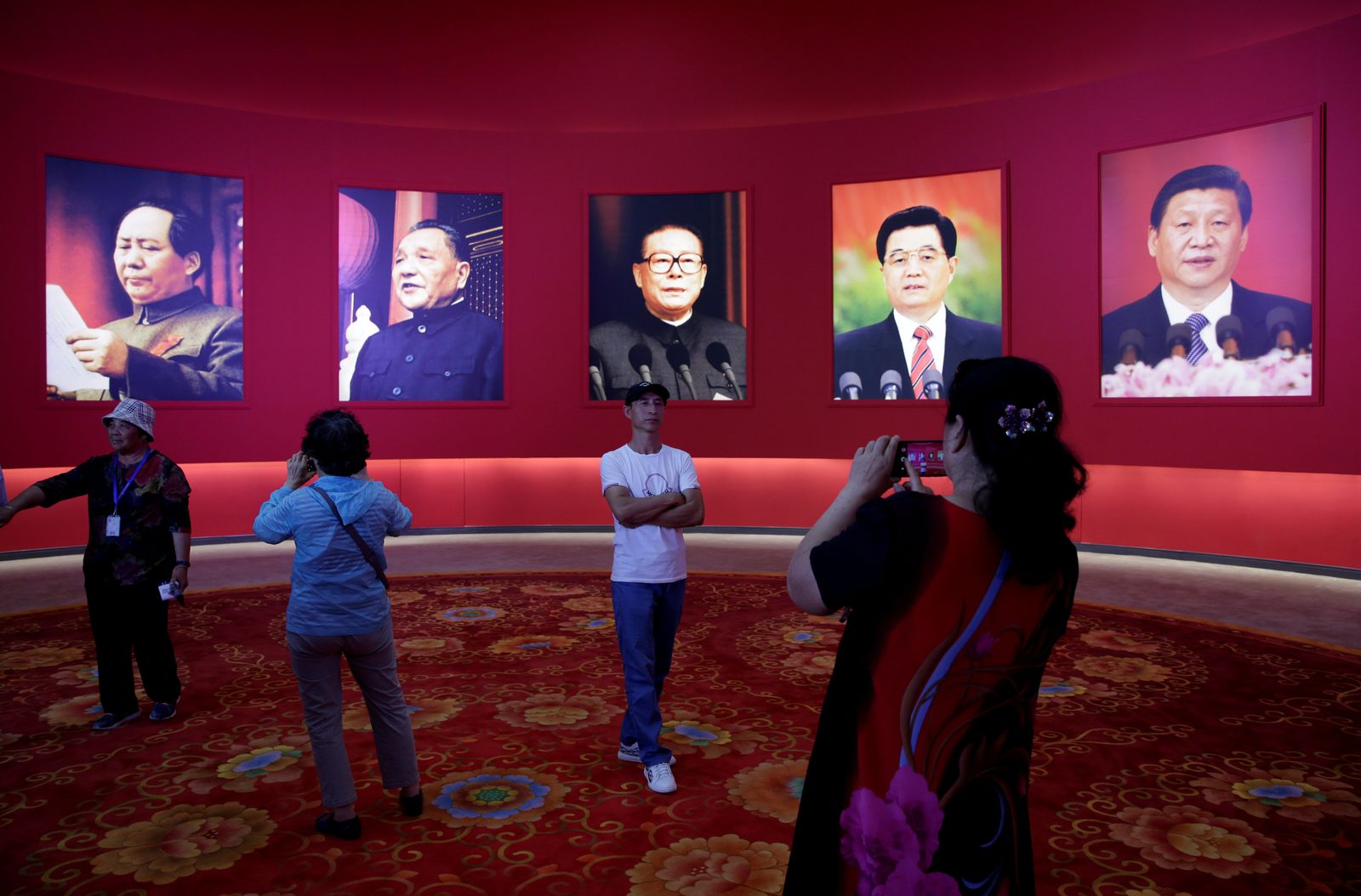 يقفون أمام صور للزعماء الصينيين، وهم (من اليمين إلى اليسار) شي جينبينغ وهو جينتاو وجيانغ زيمين ودينغ شياو بينغ وماو تسي تونغ، خلال معرض في بكين - 24 سبتمبر 2019 - REUTERS