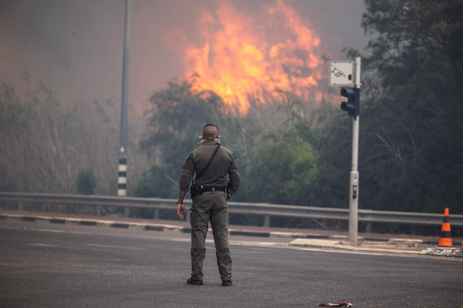 A security member stands while smoke and flame rise, as wildfires caused by extreme heat and winds broke out in central Israel, near Latrun, Israel, April 30, 2025 REUTERS/Oren Ben Hakoon ISRAEL OUT. NO COMMERCIAL OR EDITORIAL SALES IN ISRAEL.