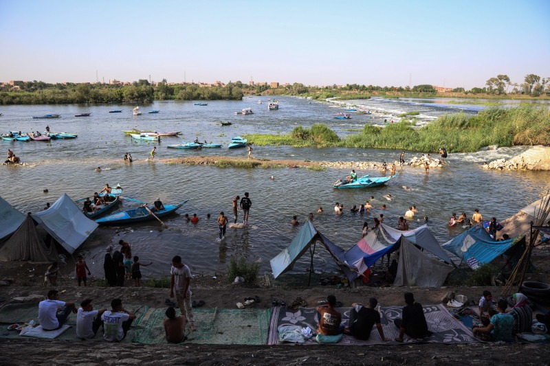 أشخاص يستظلون من الشمس، ويبردون أجسادهم بالسباحة في نهر النيل خلال موجة حر بمنطقة القناطر الخيرية، على أطراف العاصمة المصرية القاهرة