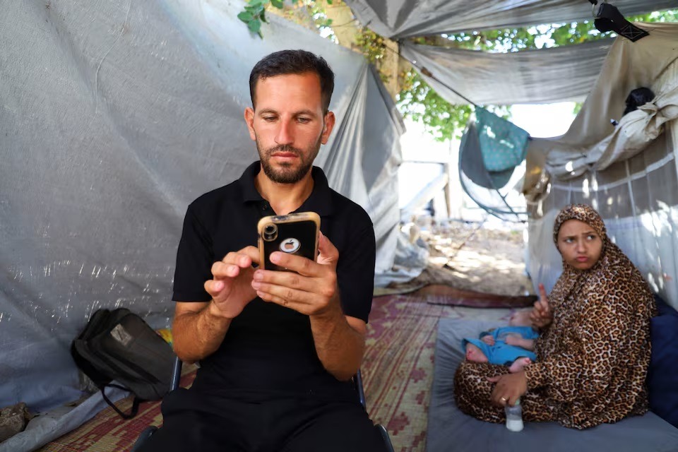 المؤثر الفلسطيني الأصم باسم الحبل يستخدم هاتفه داخل خيمته، مدينة غزة، 5 أغسطس 2025