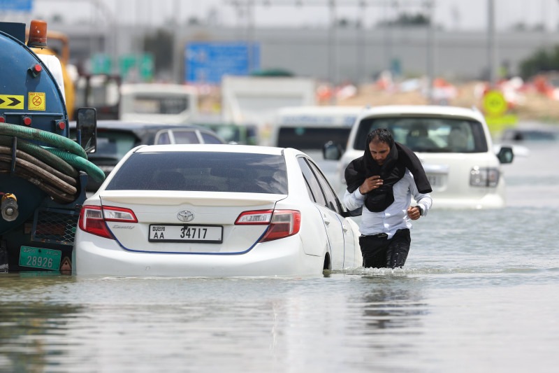 سائق يسير وسط المياه بعد أن ترك سيارته في الشارع إثر الأمطار الغزيرة في دبي