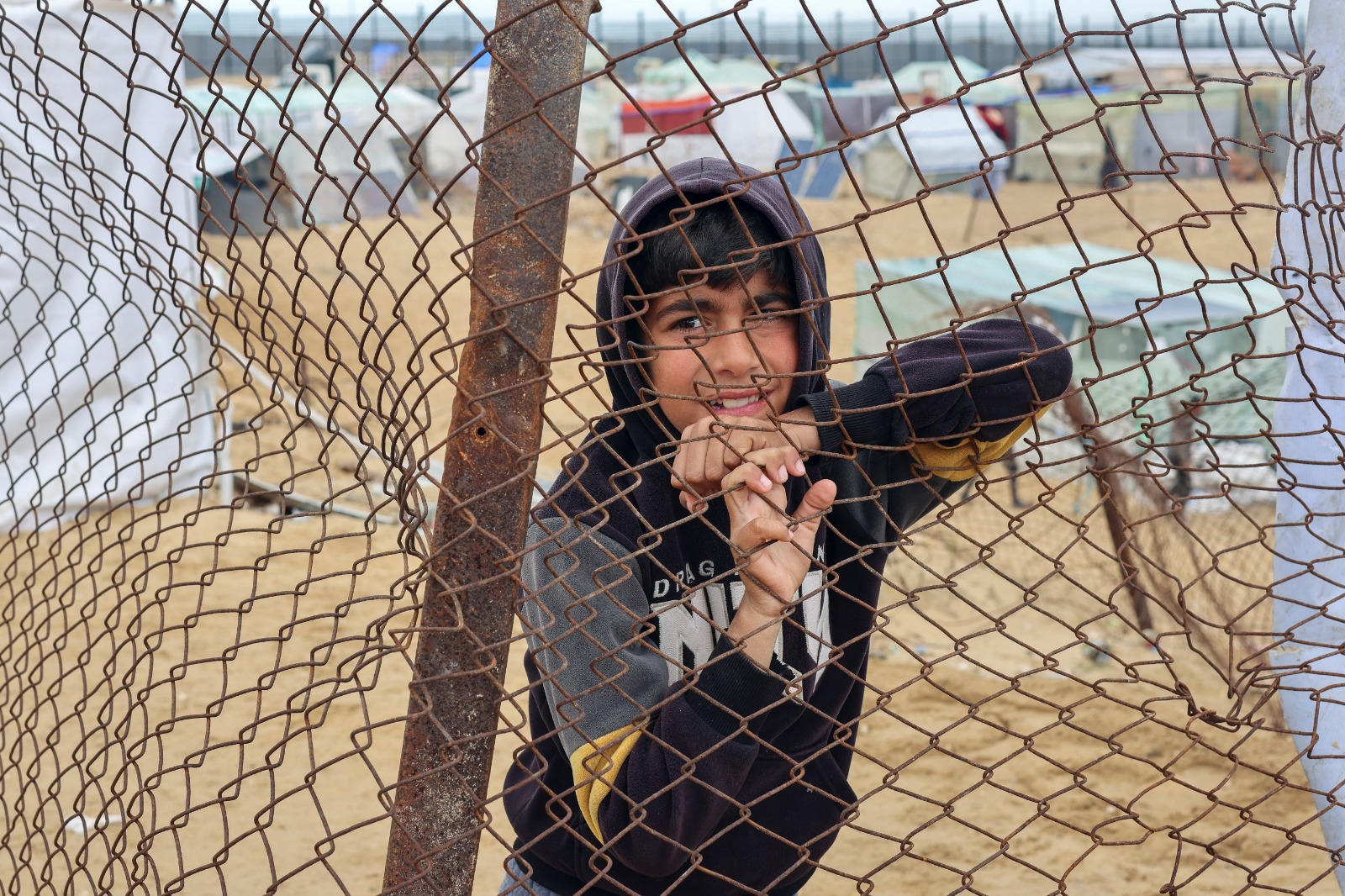 صبي فلسطيني نازح يقف بجانب سياج في مخيم على الحدود مع مصر وسط مخاوف من هجوم بري إسرائيلي على رفح، جنوب قطاع غزة. 18 فبراير 2024