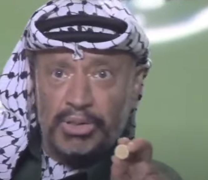 صورة من فيديو قديم تظهر الزعيم الفلسطيني الراحل ياسر عرفات وهو يمسك بقطعة نقدية إسرائيلية من فئة '10 أجورة' تحتوي على خريطة توسعات في الشرق الأوسط