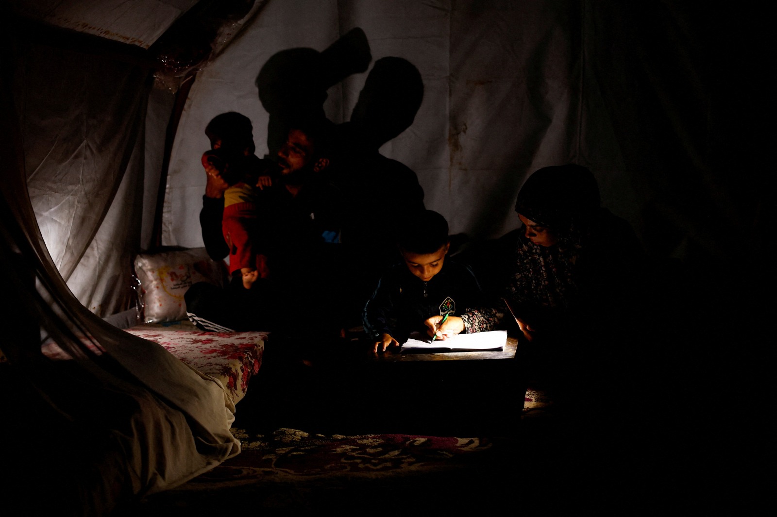 الفلسطينية حنان الجوجو تساعد طفلها في دراسته تحت ضوء مصباح يدوي داخل خيمتهم في مخيم النصيرات وسط انقطاع الكهرباء في قطاع غزة- 31 أكتوبر 2025