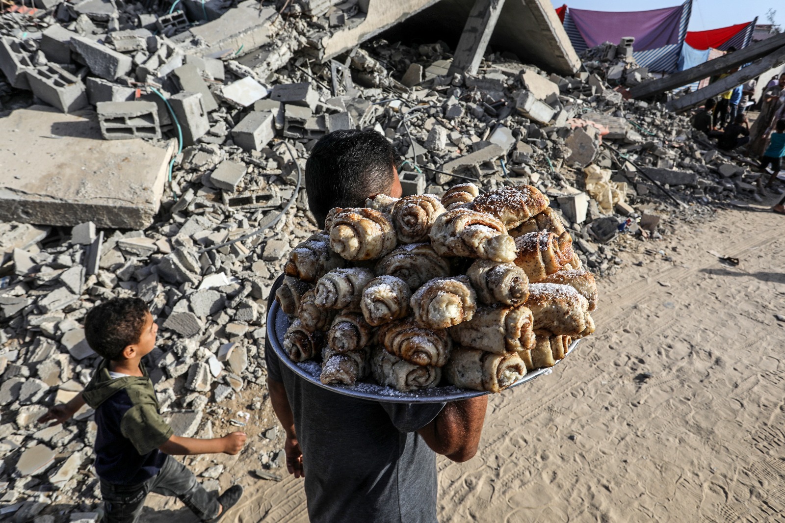 فلسطيني يوزع الكعك بمناسبة عيد الأضحى وذلك بين أنقاض المباني التي دمرتها الهجمات الإسرائيلية في خان يونس. 16 يونيو 2024