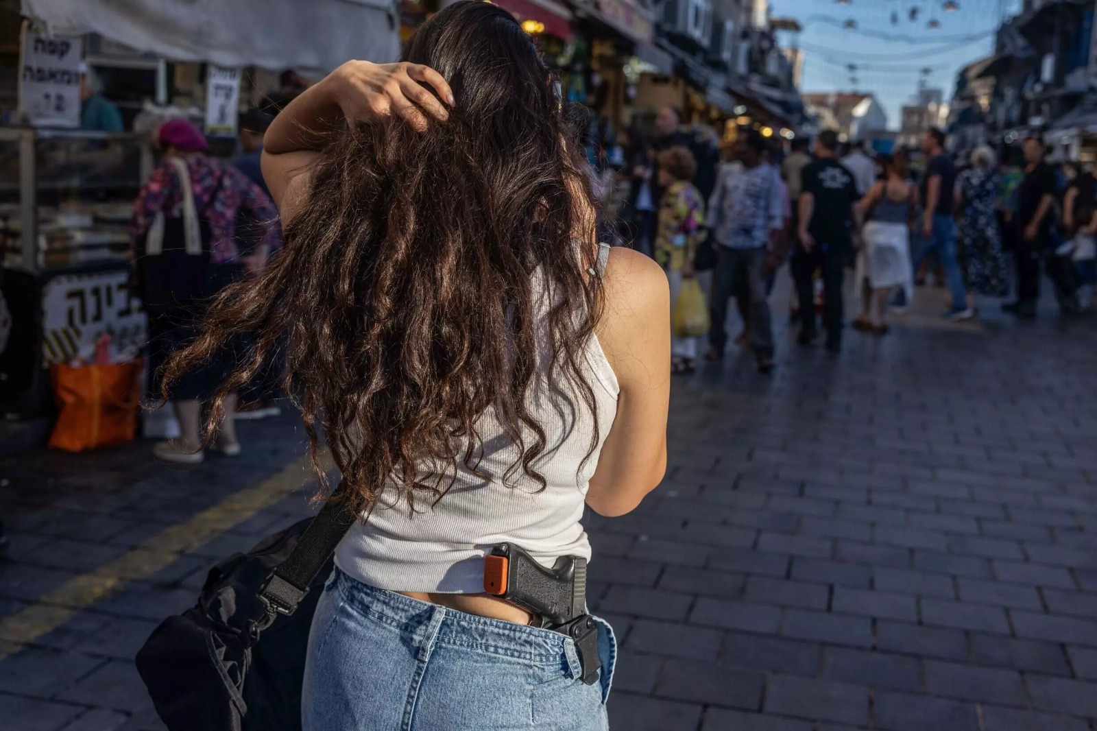 الإسرائيلية كورين نيسيم تحرص على أن يكون مسدسها ظاهراً من بنطالها عند تجولها في شوارع مدينة نتانيا شمال تل أبيب. 23 مايو 2024