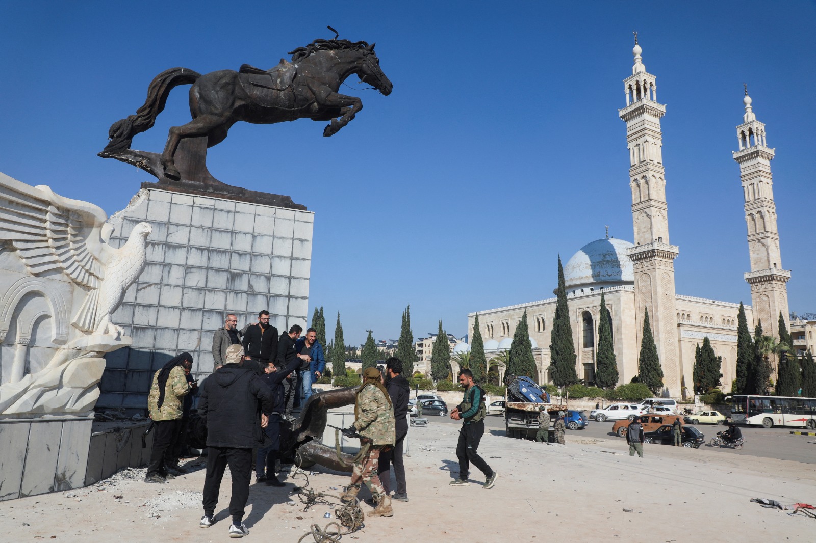 مواطنون ومقاتلون من المعارضة السورية يقفون أمام تمثال متضرر في ساحة الباسل في حلب