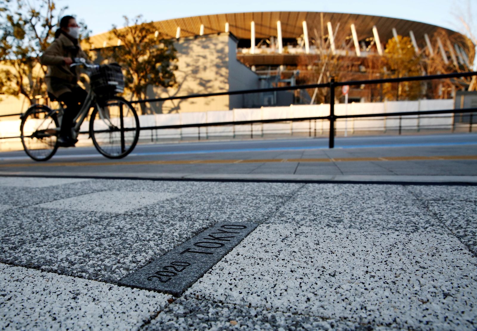 FILE PHOTO: A woman cycles past a sign for Tokyo 2020 Olympic Games on the pavement in front of the National Stadium, the main stadium of Tokyo 2020 Olympics and Paralympics, in Tokyo - REUTERS