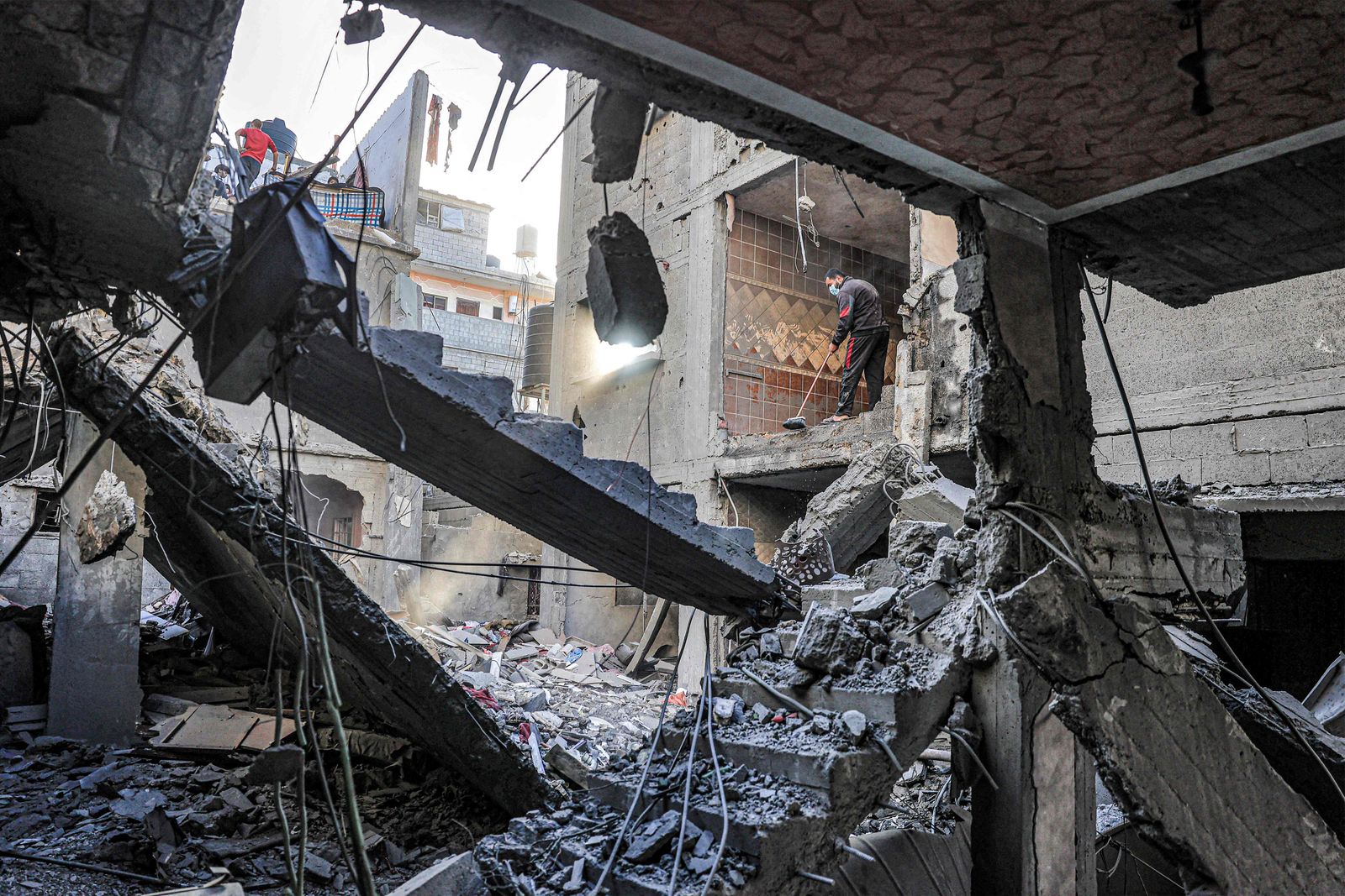 A man sweeps a room with an empty wall overlooking a building destroyed by Israeli bombardment in Rafah in the southern Gaza Strip on December 24, 2023 amid the ongoing conflict between Israel and the militant group Hamas. (Photo by SAID KHATIB / AFP)