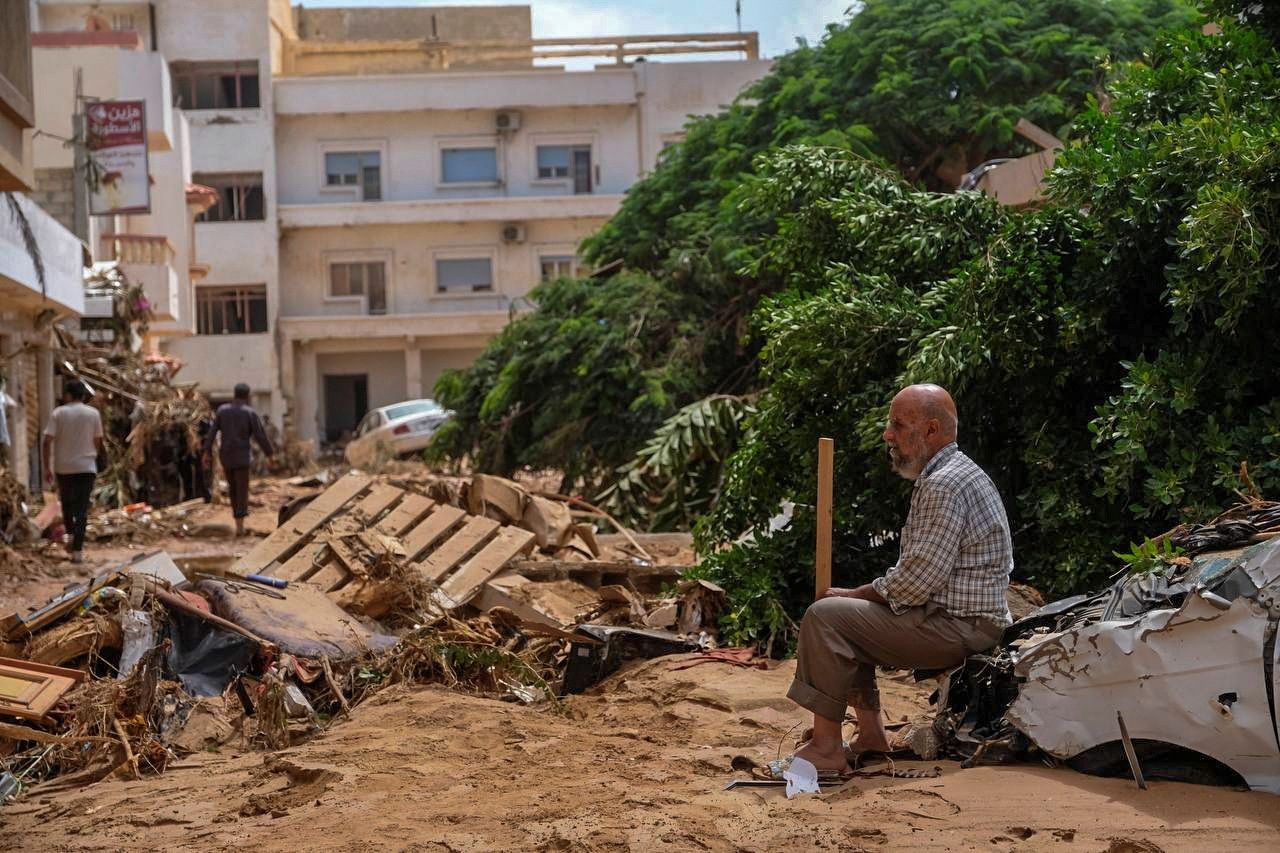  رجل يجلس فوق سيارة متضررة جرّاء العاصفة 