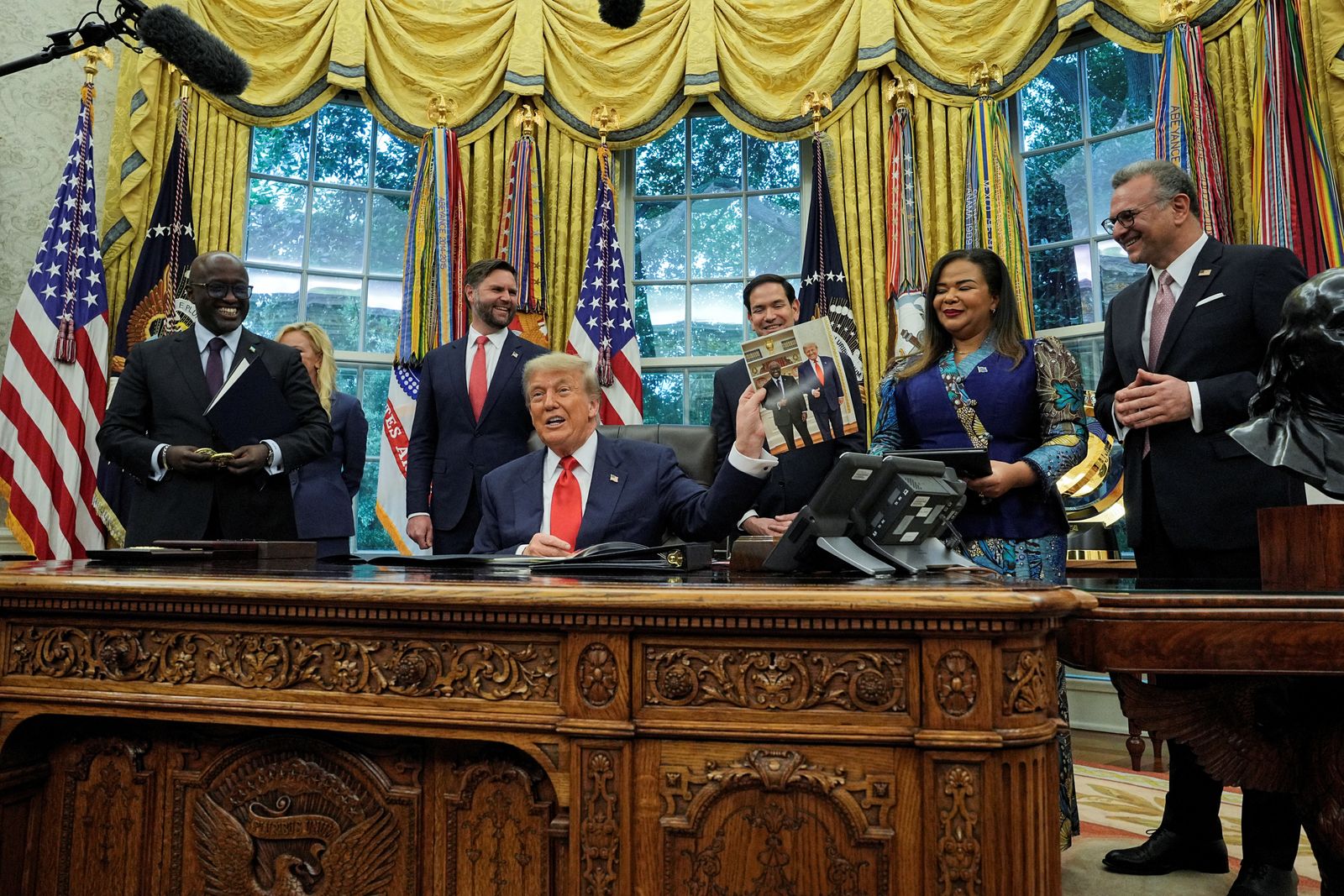 U.S. President Donald Trump holds a picture of himself with Rwanda's Foreign Minister Olivier Nduhungirehe, during a meeting with Foreign Minister Nduhungirehe and the Democratic Republic of the Congo's Foreign Minister Therese Kayikwamba Wagner in the Oval Office at the White House in Washington, D.C., June 27, 2025. REUTERS/Ken Cedeno