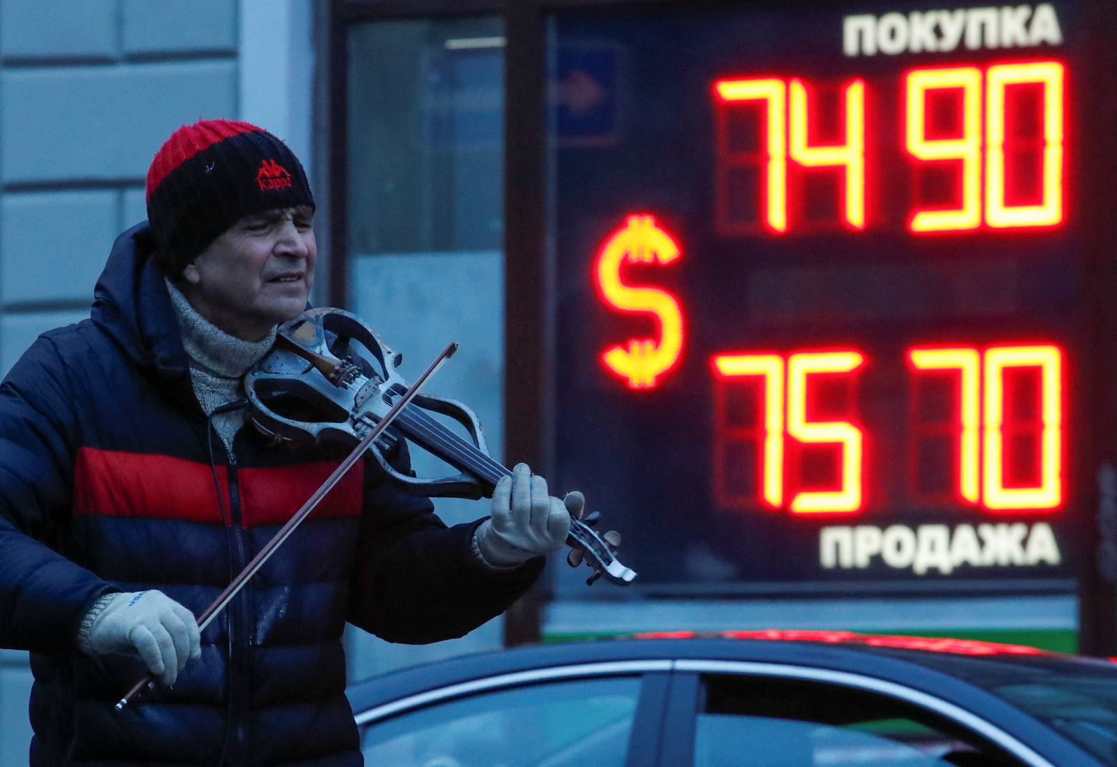 يعزف على الكمان قرب لوحة تعرض سعر صرف الدولار في مقابل الروبل الروسي بسان بطرسبرج - 16 فبراير 2022 - REUTERS