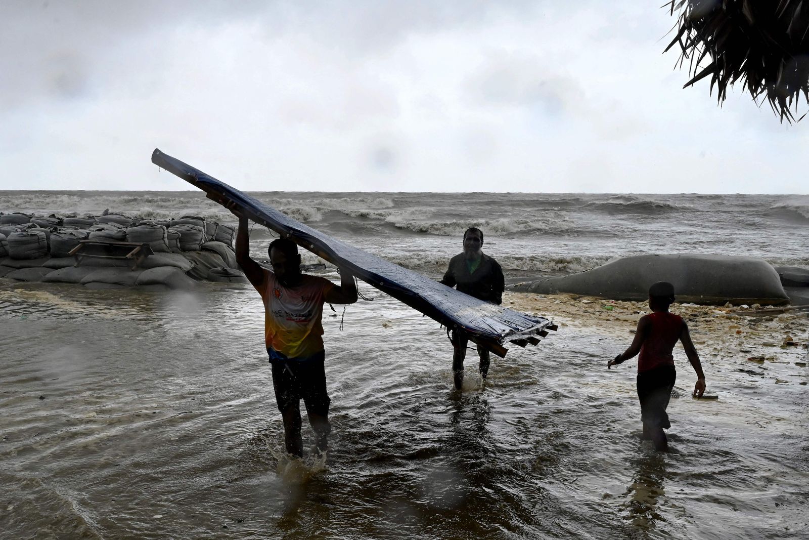 A man (L) carries parts of his makeshift shop to a sea shore as a preventive measure during rainfall in Kuakata on May 26, 2024, ahead of cyclone Remal's landfall in Bangladesh. Cyclone Remal is set to hit the country and parts of neighbouring India on May 26 evening, with Bangladesh's weather department predicting crashing waves and howling gales with gusts of up to 130 kilometres (81 miles) per hour. (Photo by Munir UZ ZAMAN / AFP)