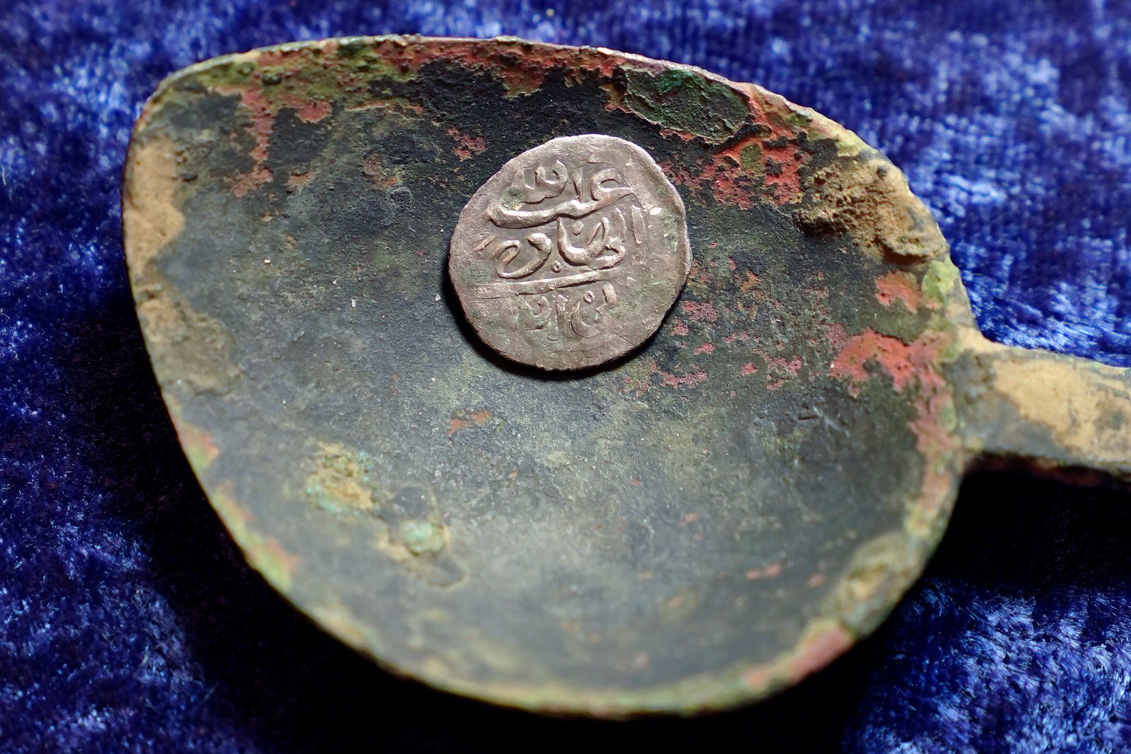 A 17th century Arabian silver coin that research shows was struck in 1693 in Yemen, rests in a 17th century brass spoon on a table, in Warwick, R.I., Thursday, March 11, 2021. The coin was found at a farm, in Middletown, R.I., in 2014 by metal detectorist Jim Bailey, who contends it was plundered in 1695 by English pirate Henry Every from Muslim pilgrims sailing home to India after a pilgrimage to Mecca. (AP Photo/Steven Senne) - AP
