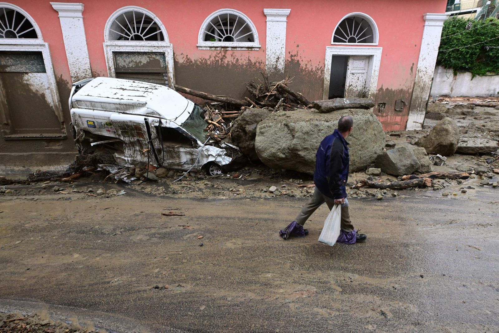 ساكن محلي يسير بجوار سيارة متضررة مدمرة بعد هطول أمطار غزيرة تسببت في انهيار أرضي بجزيرة إيسكيا جنوبي إيطاليا- 26 نوفمبر 2022 - AFP