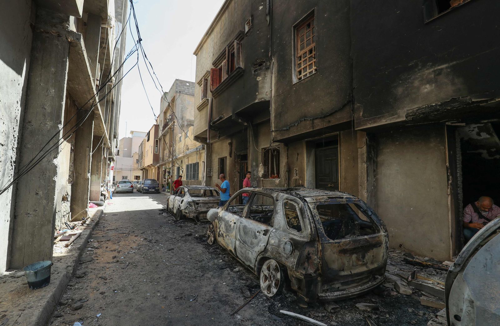 People inspect car carcasses following clashes between backers of rival governments in Libya's capital Tripoli, on August 28, 2022. - Flights resumed and shops re-opened in Libya's capital after clashes between backers of rival governments killed at least 32 people and sparked fears of major new conflict. (Photo by Mahmud TURKIA / AFP) - AFP