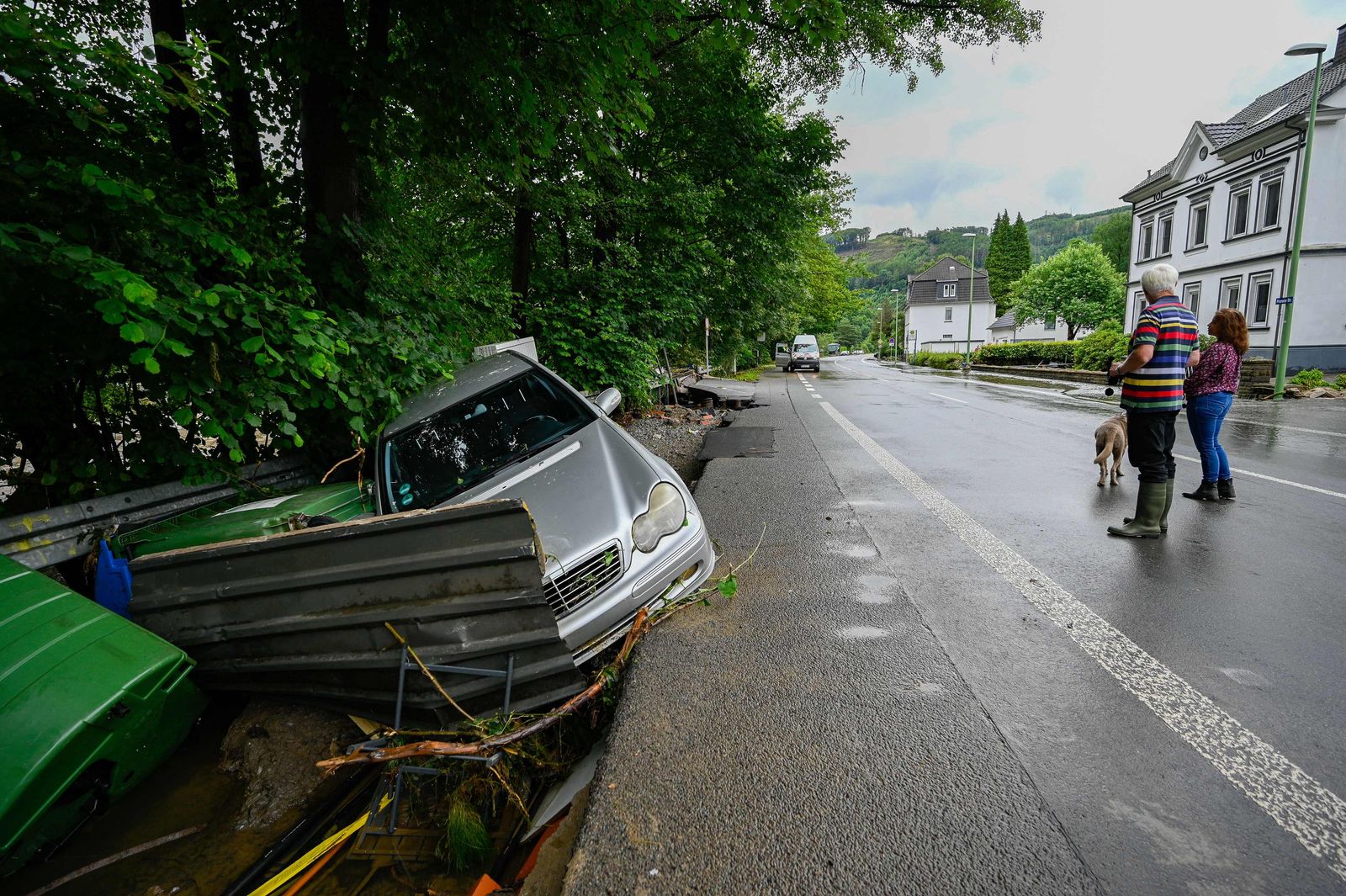 People look a at a destroyed car and other damages caused by the floods of the Volme river on July 15, 2021 in Priorei near Hagen, western Germany, after heavy rain hit parts of the country, causing widespread flooding. - Heavy rains and floods lashing western Germany have killed at least nine people and left around 50 missing, as rising waters led several houses to collapse, police said. (Photo by SASCHA SCHUERMANN / AFP) - AFP