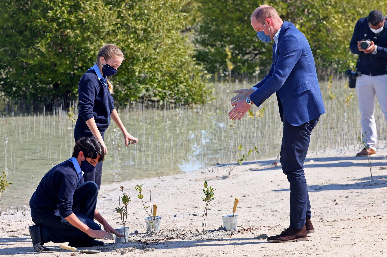 Britain's Prince William, Duke of Cambridge, plants trees alongside two school children as he tours Abu Dhabi's wetlands at the Jubail Magrove Park during an official visit to the United Arab Emirates (UAE) on February 10, 2022. - Prince William's climate-focused visit also aims to bolster ties between the two countries after the UAE, a former British protectorate, marked 50 years since its founding in 1971. (Photo by Giuseppe CACACE / AFP) - AFP