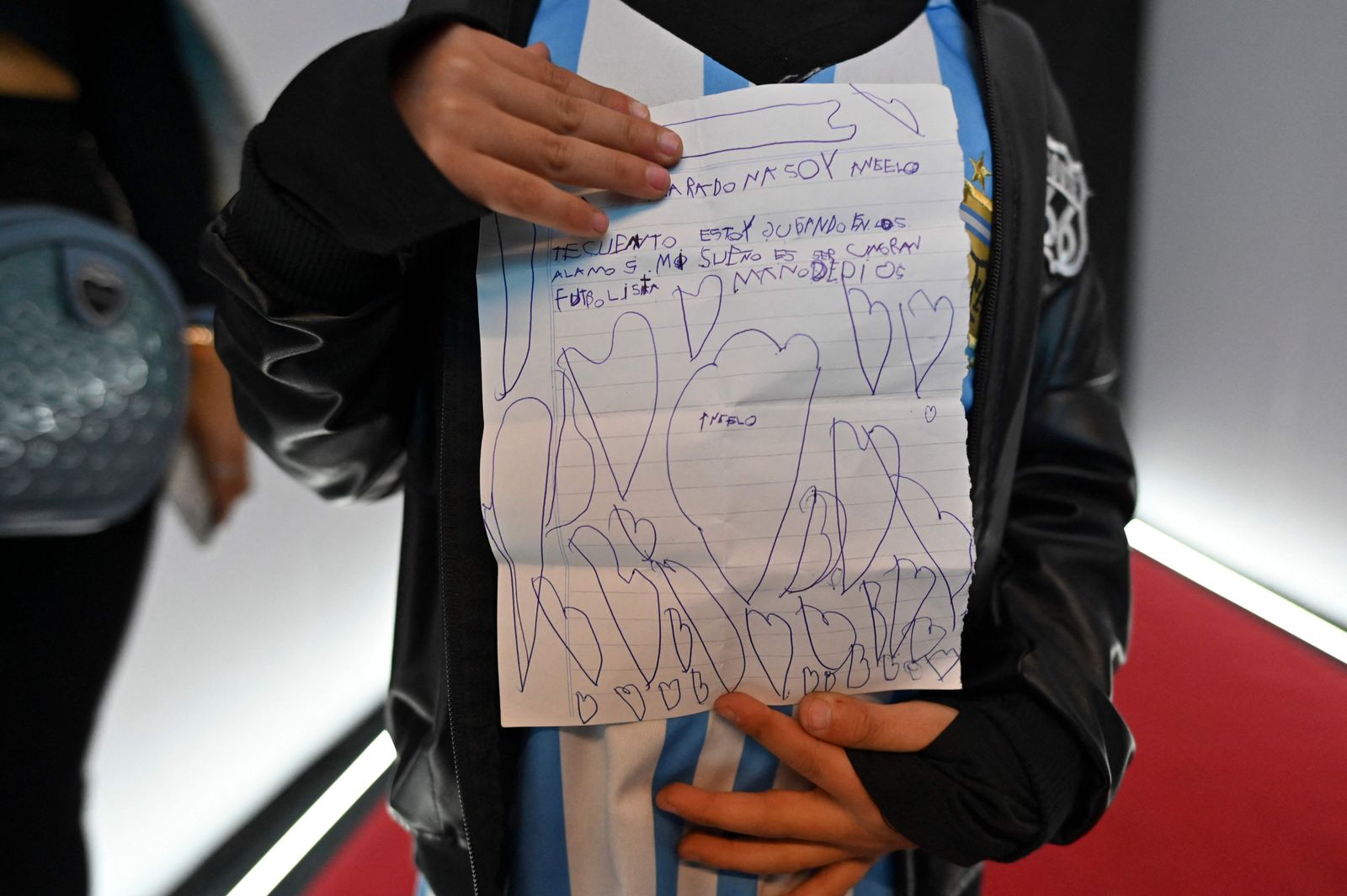 A boy holds a letter that he wrote to Argentine late football star Diego Armando Maradona, before recording a message to him, at the aerodrome of Moron, Buenos Aires province, Argentina, on July 23, 2022. - Followers of Maradona recorded videos with messages to the soccer star, that will be saved on a hard drive and sent to a satellite that will orbit the planet earth and can be monitored by Maradona's followers, which they call 