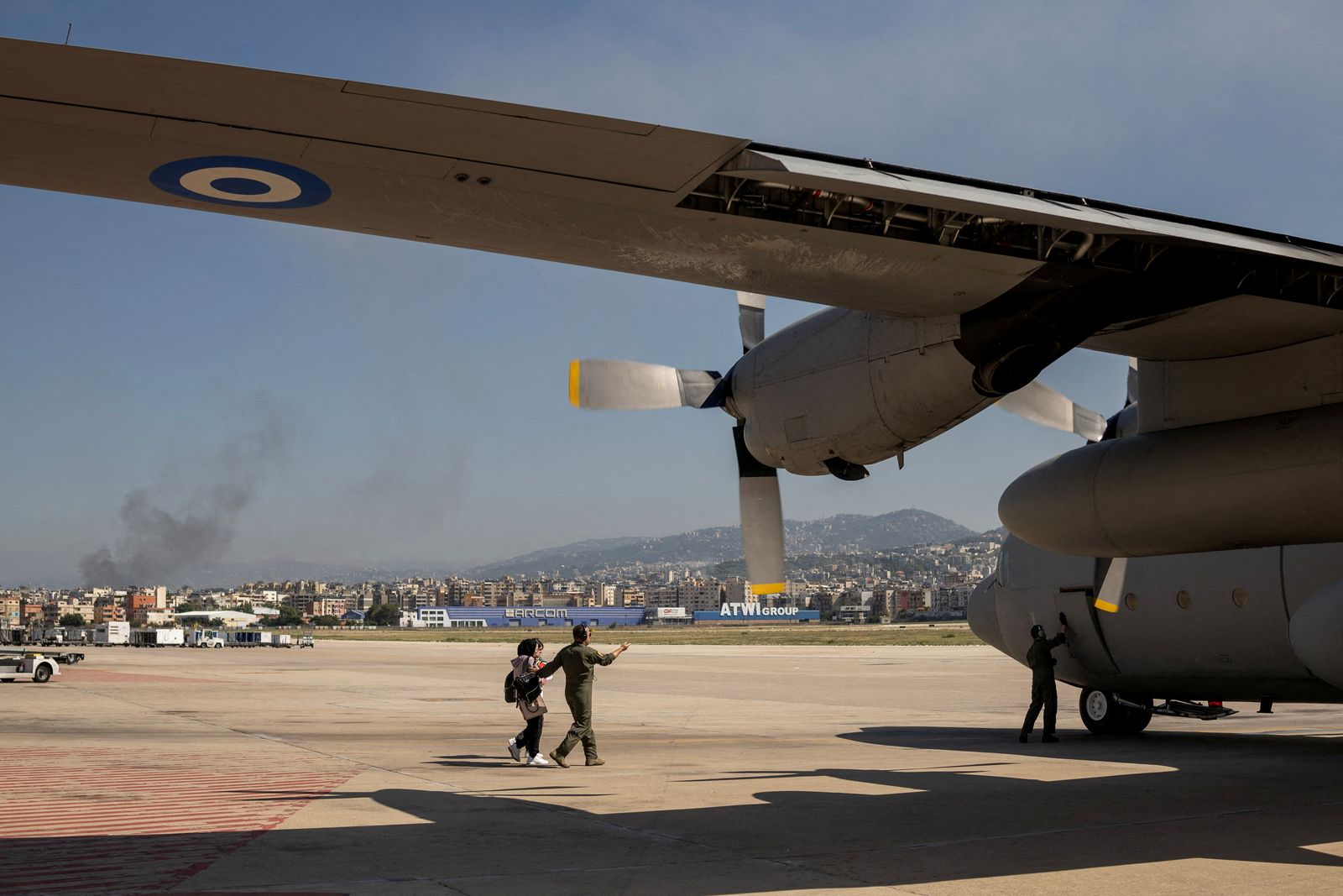 Smoke rises from Beirut's southern suburbs as a crew member helps two women and a baby to board a Hellenic Air Force C130 during the evacuation of Greek and Greek Cypriot nationals from Lebanon, due to ongoing hostilities between Hezbollah and the Israeli forces, in Beirut, Lebanon, October 3, 2024. REUTERS/Alkis Konstantinidis     TPX IMAGES OF THE DAY