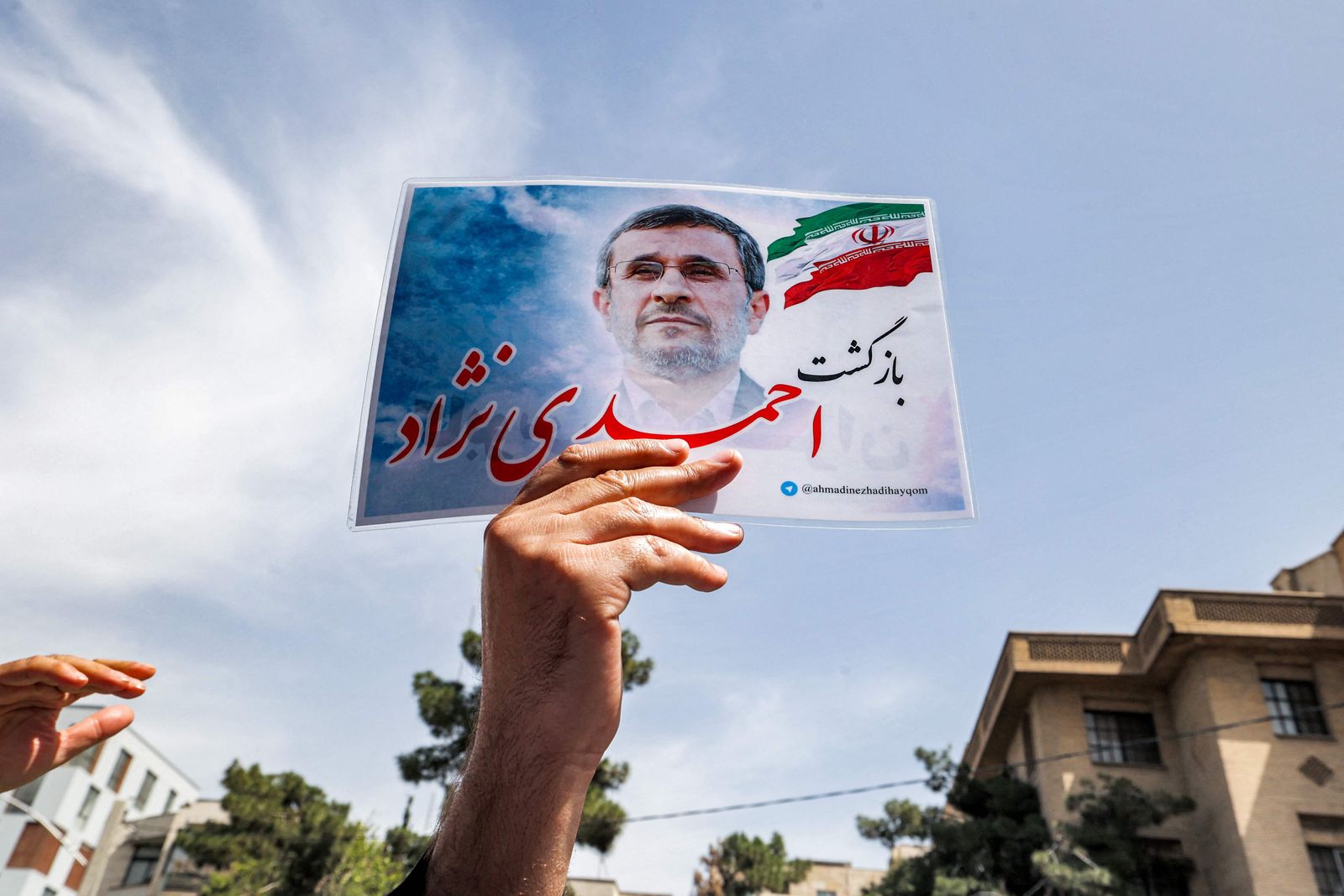 A supporter of Iran's former president Mahmoud Ahmadinejad holds up a flyer bearing his image outside the Interior Ministry headquarters in the capital Tehran on May 12, 2021 as Ahmadinejad arrives to register his candidacy to run again for the presidential elections scheduled for June. (Photo by ATTA KENARE / AFP) - AFP