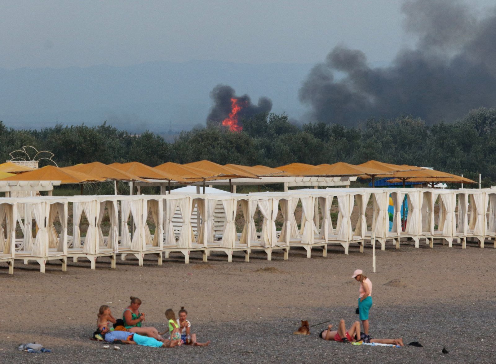 People rest on a beach as smoke and flames rise after explosions at a Russian military airbase, in Novofedorivka - REUTERS