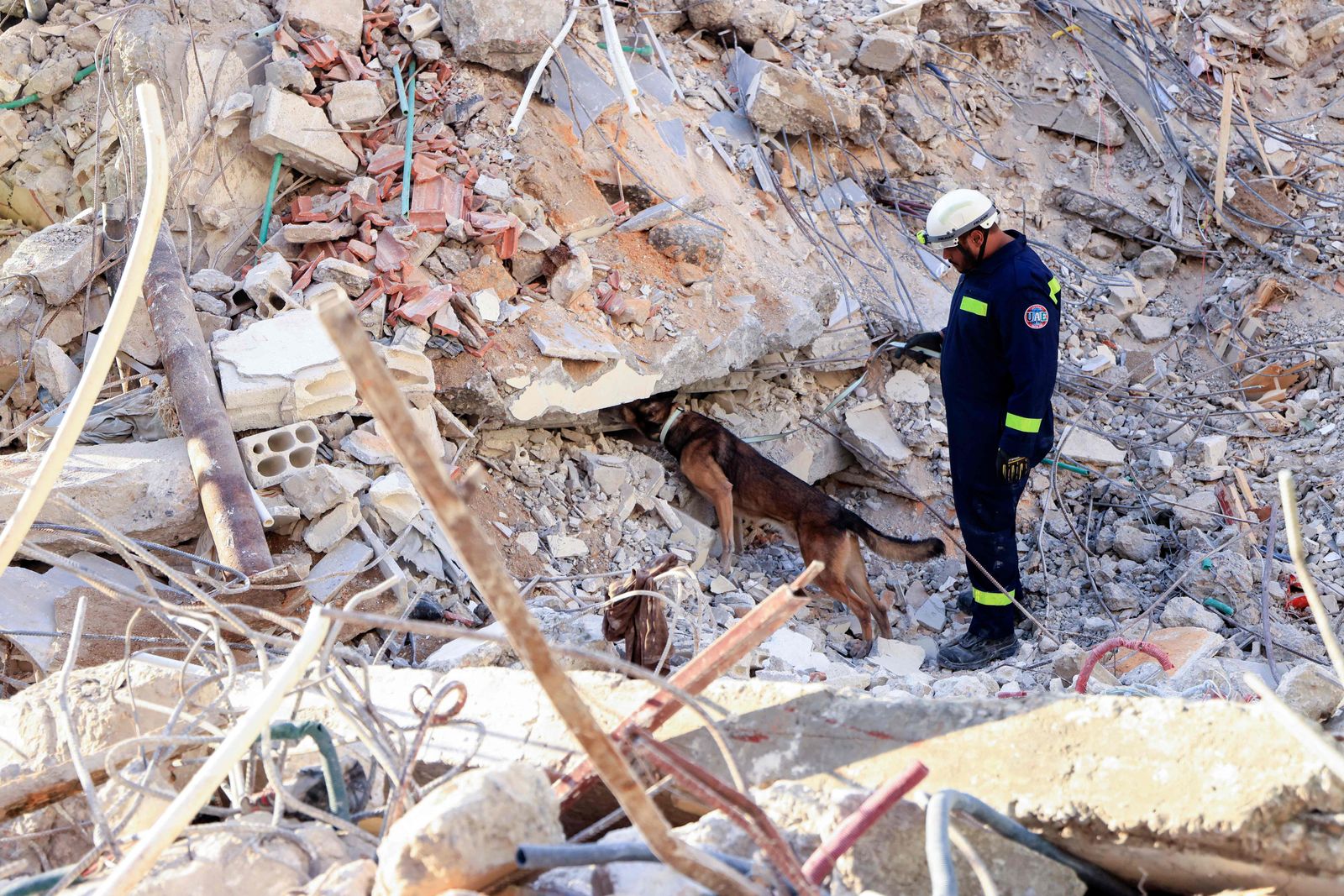 An Emirati rescuer, with the help of a dog, searches for victims amidst the rubble of a collapsed building in the regime-controlled town of Jableh in the province of Latakia, northwest of the Syrian capital, on February 11, 2023, in the aftermath of a deadly earthquake. - Aftershocks following the February 6 earthquake of 7.8-magnitude in Turkey and Syria, have added to the death toll and further upended the lives of survivors. (Photo by Karim SAHIB / AFP) - AFP