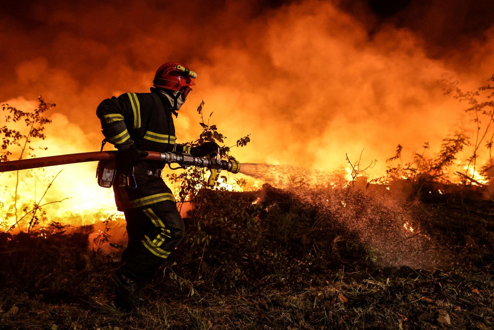 A firefighter supported by tactical firefighters (unseen) set controlled fires to burn a plot of land as they attempt to prevent the wild fire from spreading due to wind change, as they fight a forest fire near Louchats in Gironde, southwestern France on July 17, 2022. - France was on high alert on July 18, 2022, as the peak of a punishing heatwave gripped the country, while wildfires raging in parts of southwest Europe showed no sign of abating. In the southwestern Gironde region, firefighters over the weekend continued to fight to control forest blazes that have devoured nearly 11,000 hectares (27,000 acres) since July 12. (Photo by THIBAUD MORITZ / AFP) - AFP