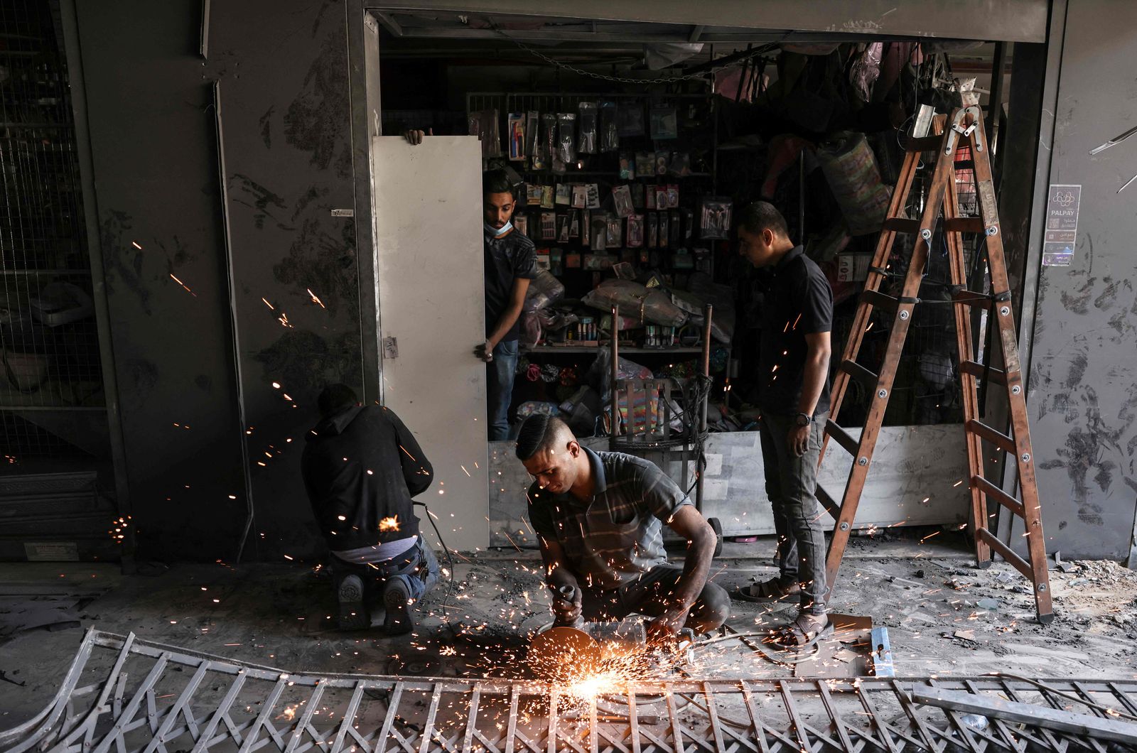 Palestinian labourers fix a damaged store at a shopping center, next to a building that was hit by an Israeli strike, in Gaza City on May 22, 2021. (Photo by MAHMUD HAMS / AFP) - AFP