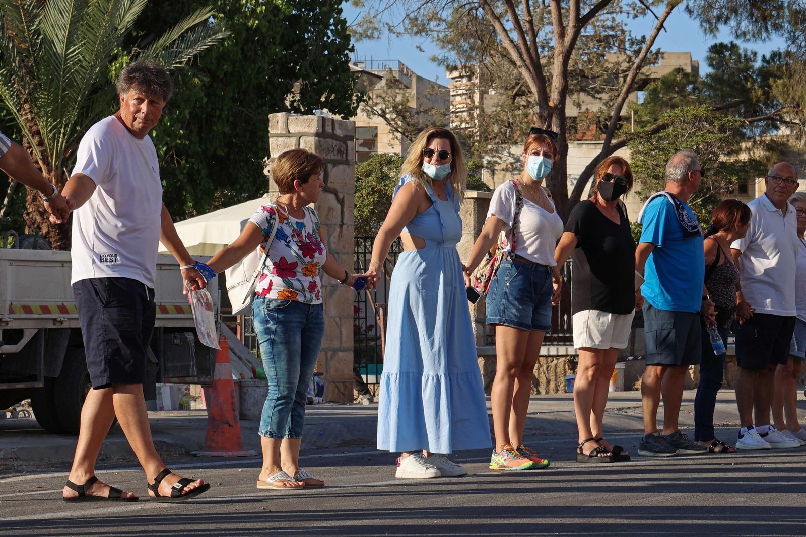 Nikos Karoullas (L) takes part in the human chain for xxx  in the fenced-off area of Varosha in Famagusta town in the self-proclaimed Turkish Republic of Northern Cyprus (TRNC) of the divided Mediterranean island of Cyprus, on July 16, 2021. - Turkish President Recep Tayyip Erdogan heads to breakaway north Cyprus Tuesday, to mark the anniversary of Turkey's 1974 invasion, a visit infuriating Greek Cypriots with island reunification talks in limbo. (Photo by Christina ASSI / AFP) - AFP