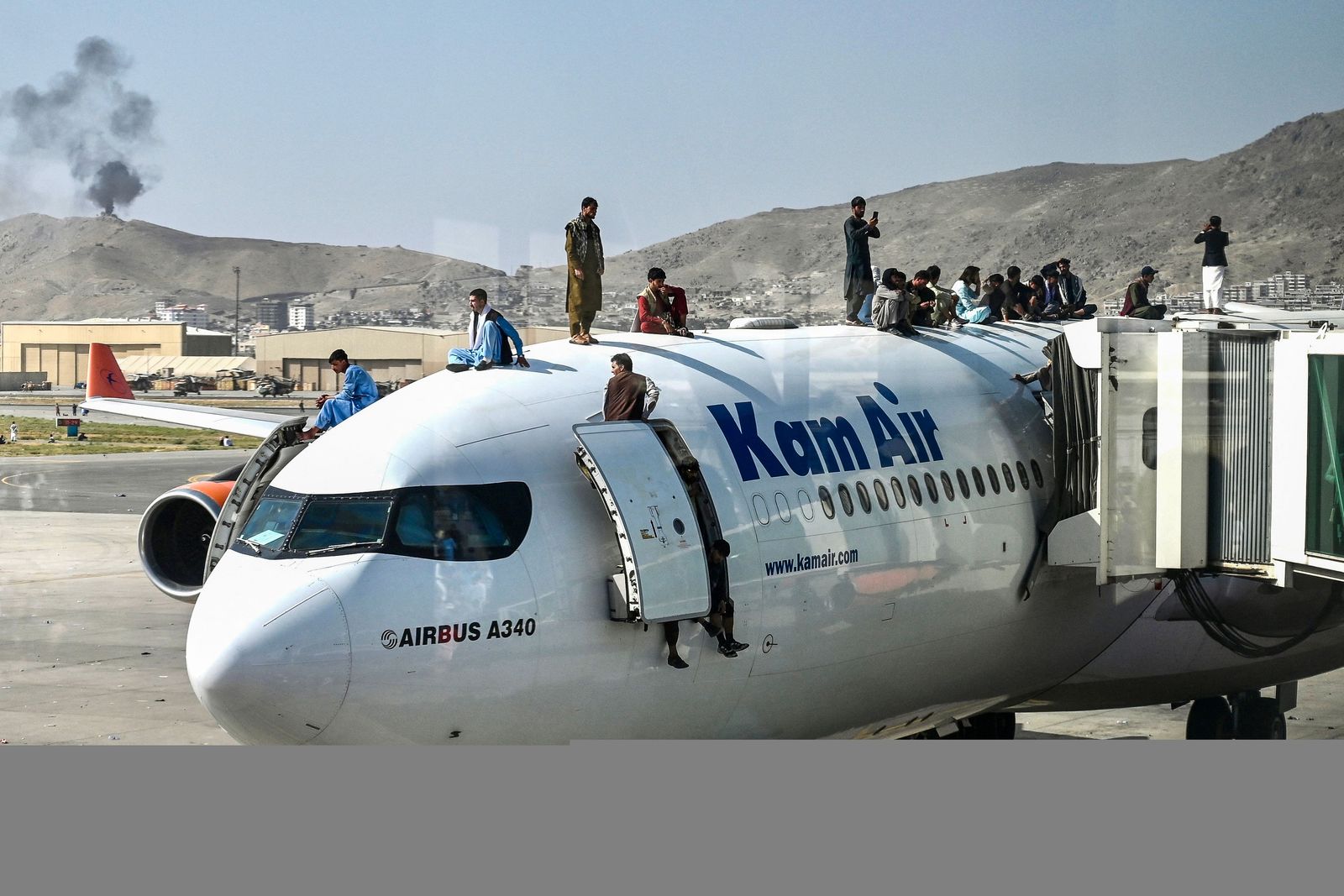 Afghan people climb atop a plane as they wait at the airport in Kabul on August 16, 2021, after a stunningly swift end to Afghanistan's 20-year war, as thousands of people mobbed the city's airport trying to flee the group's feared hardline brand of Islamist rule. (Photo by Wakil Kohsar / AFP) - AFP