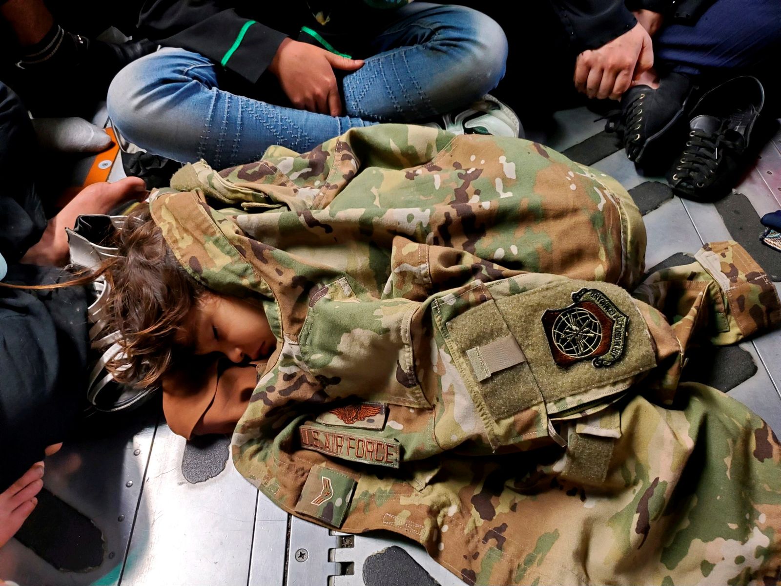 طفل أفغاني ينام على أرضية الشحن في طائرة تابعة للقوات الجوية الأمريكية، مغطى بزي الطيار من الدرجة الأولى نيكولاس بارون ، مسؤول تحميل C-17 ، أثناء رحلة إجلاء من كابول- 18 أغسطس 2021 - U.S. Central Command Public Affa