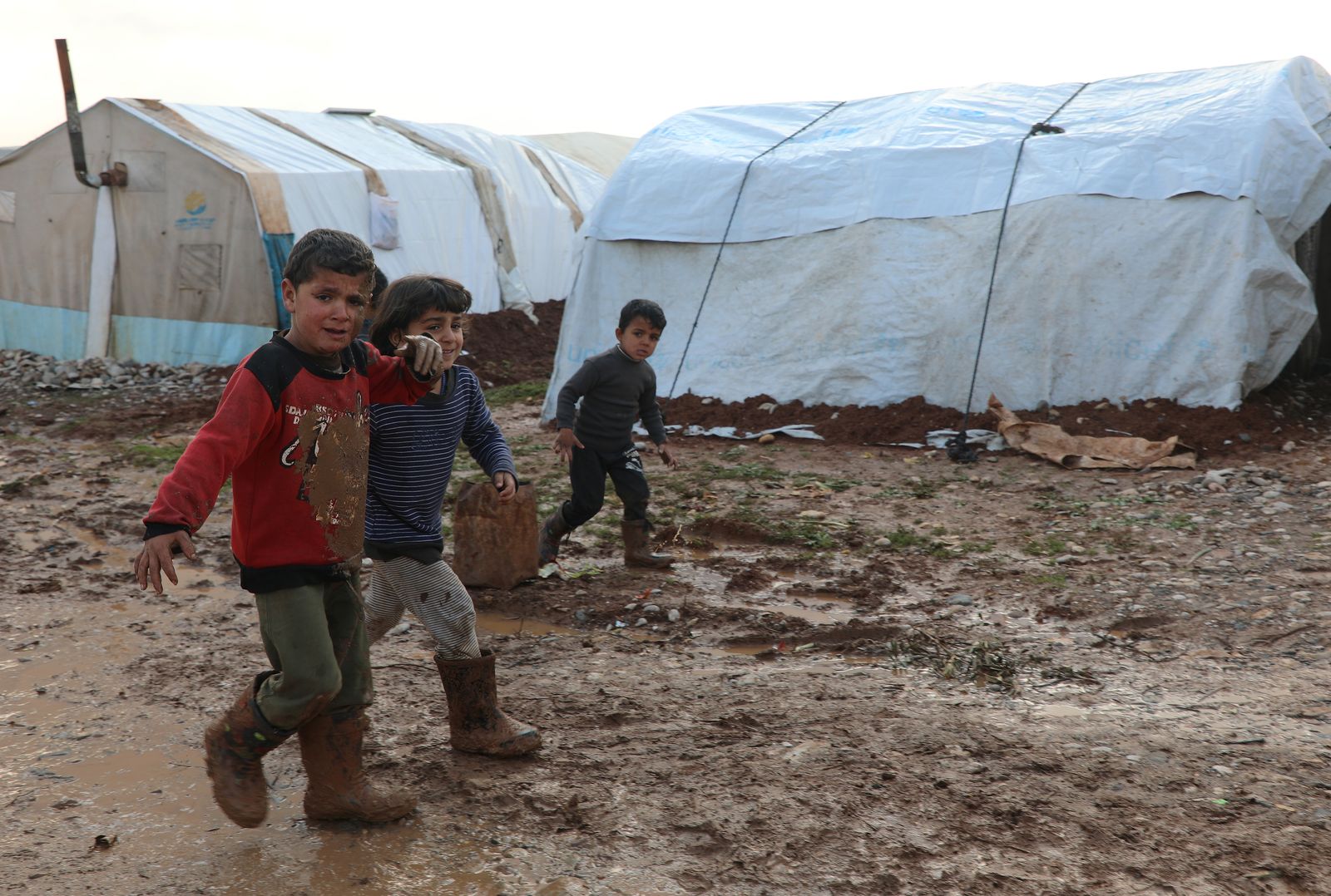 أطفال سوريون يسيرون في الوحل بأحد مخيمات اللاجئين في ريف حلب الشمالي- 20 يناير 2021 - REUTERS