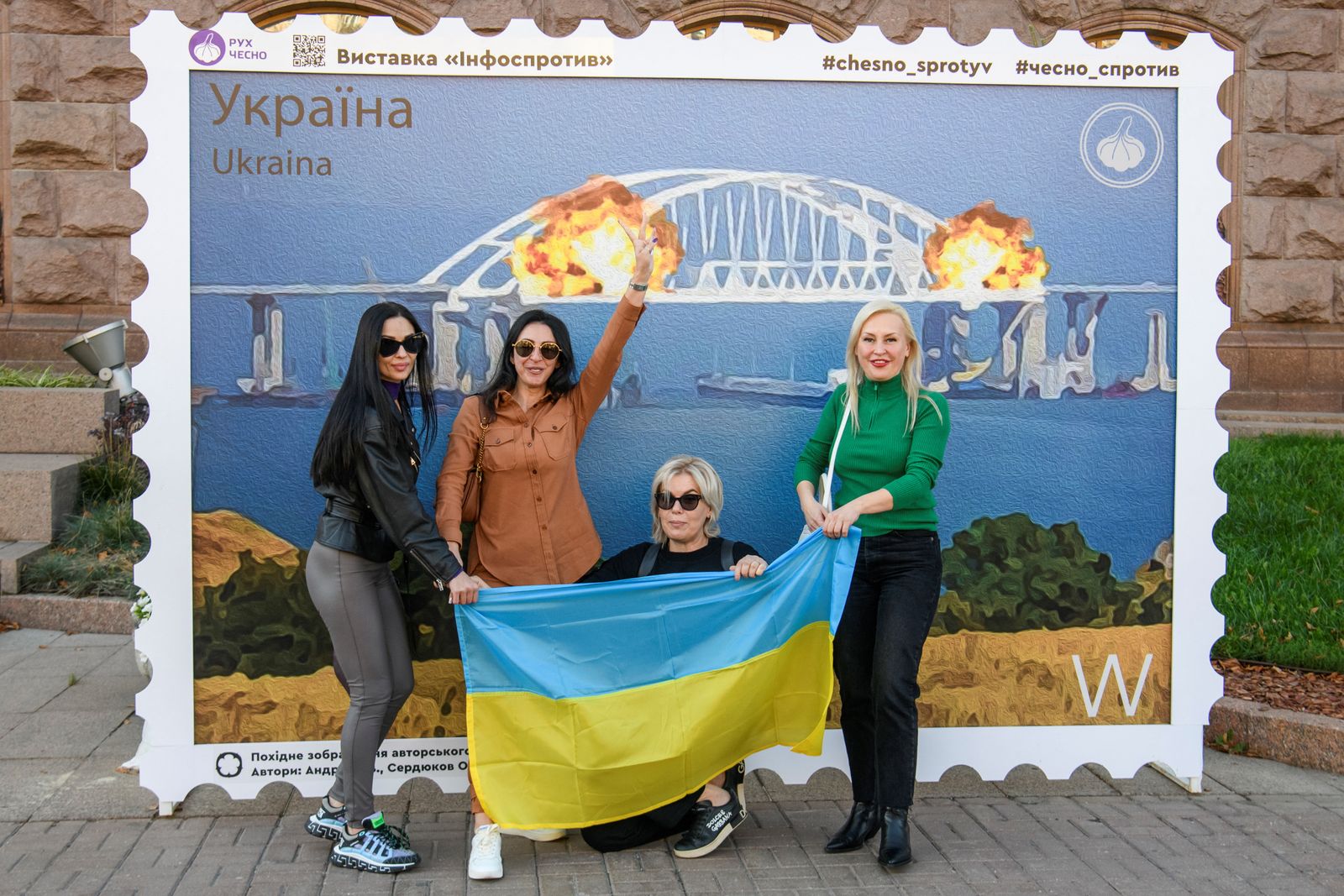 Women pose with Ukrainian national flag next to an artwork depicting Kerch bridge on fire, in Kyiv - REUTERS