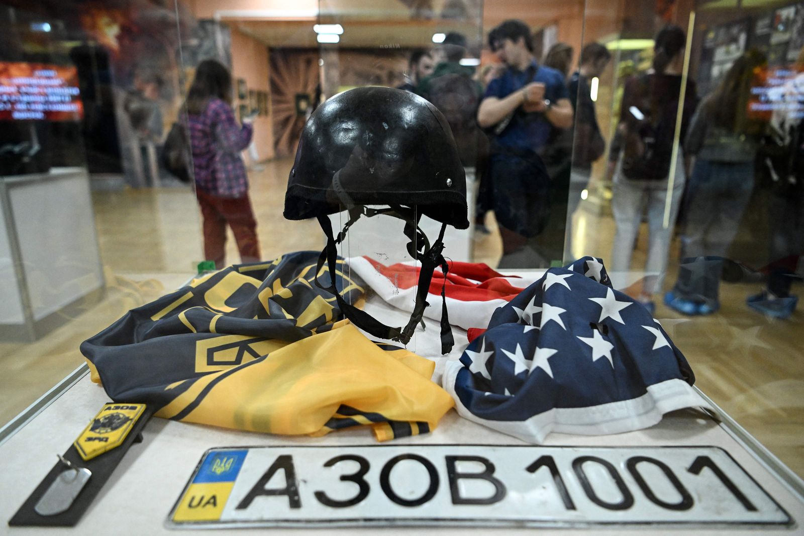 Visitors pass by a glass cabinet with a Ukrainian car plate past a US flag at an exhibition as she visit the exhibition 