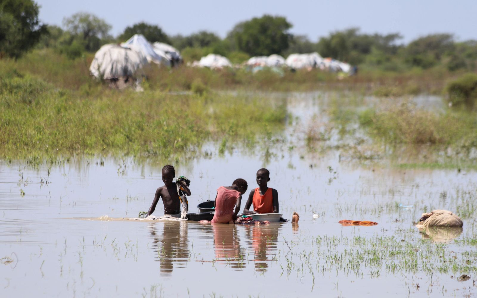 أطفال نازحون ينظفون ملابسهم داخل مياه الفيضانات في إحدى مناطق السودان - REUTERS