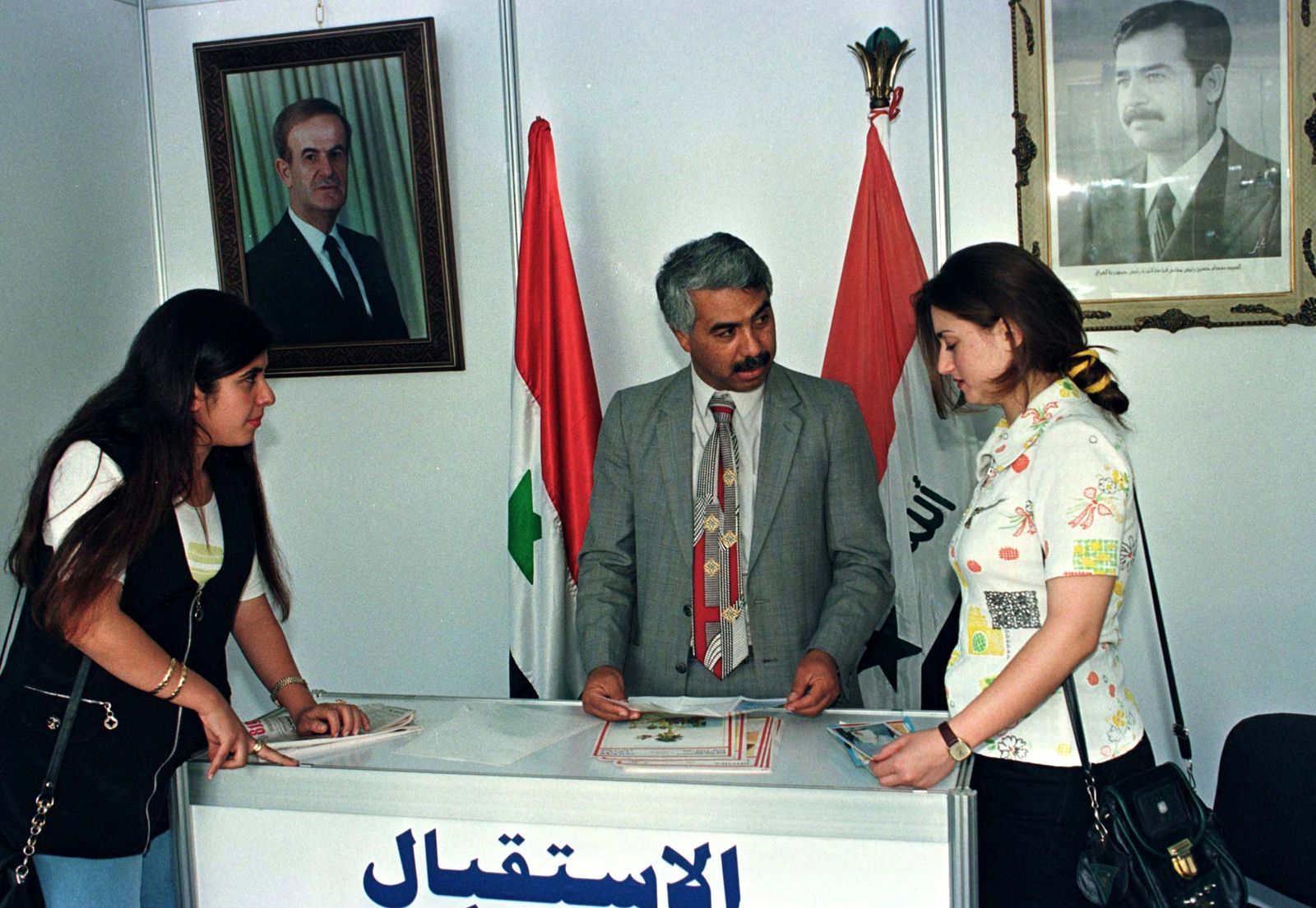 نساء سوريات يطلعن على مقالات عراقية خلال افتتاح المعرض التجاري الدولي بدمشق في 28 أغسطس 1997. ويعرض العراق منتجاته في سوريا لأول مرة منذ 17 عاماً. وعلى الحائط صور الرئيس السوري حافظ الأسد والرئيس العراقي صدام حسين - REUTERS
