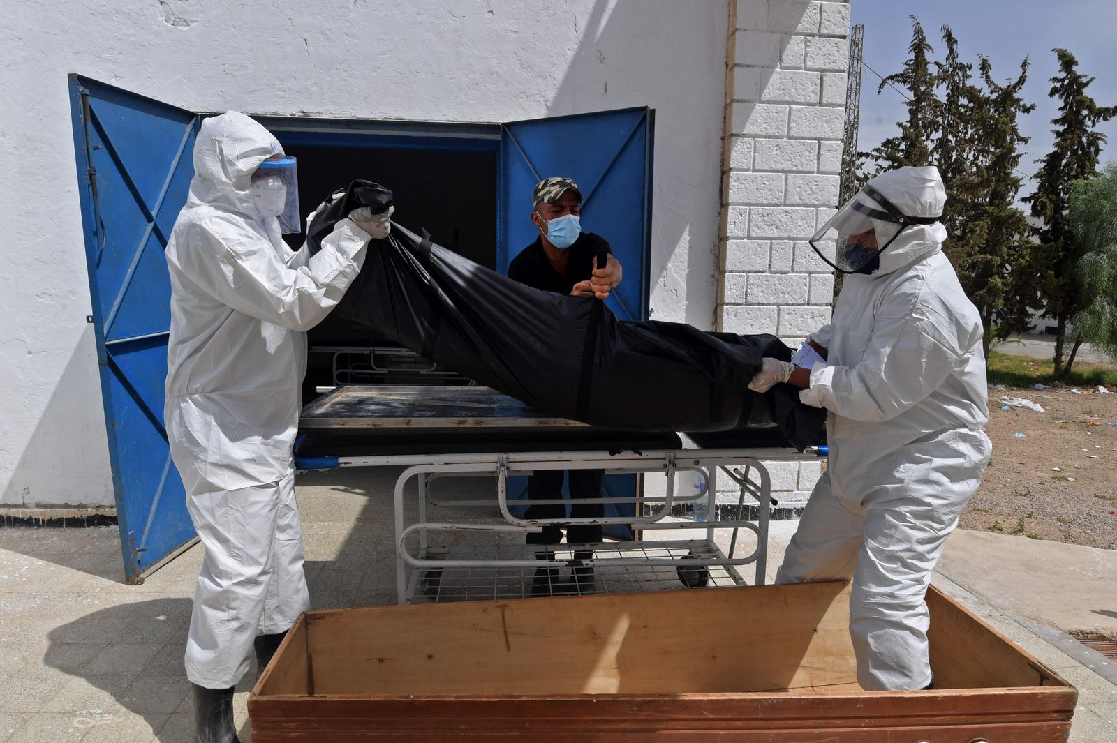 Tunisian municipality employees place the body of a COVID-19 victim into a casket at the Ibn al-Jazzar hospital in the east-central city of Kairouan on July 4, 2021. - Tunisia placed the capital Tunis and the northern town of Bizerte under a partial lockdown from until July 14 in a bid to rein in record daily coronavirus cases and deaths. (Photo by FETHI BELAID / AFP) - AFP