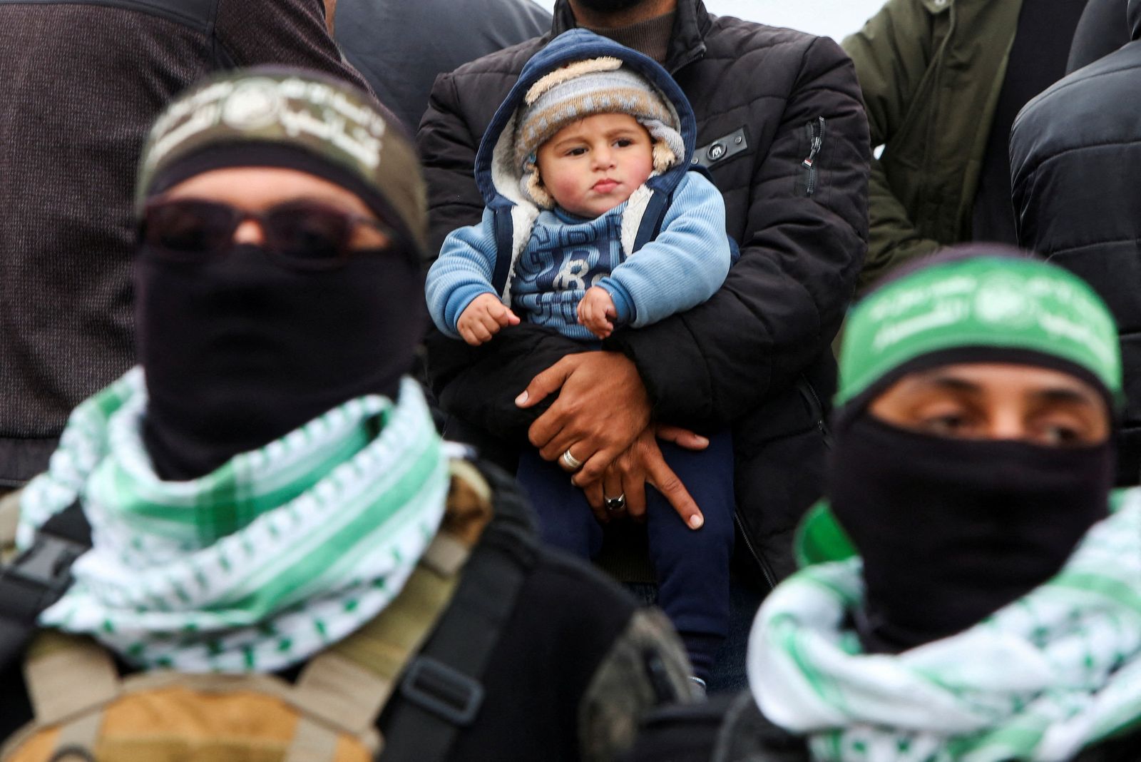 A Palestinian man with a child looks on as Hamas militants stand guard on the day Hamas hands over deceased hostages Oded Lifschitz, Shiri Bibas and her two children Kfir and Ariel Bibas, seized during the deadly October 7, 2023 attack, to the Red Cross, as part of a ceasefire and hostages-prisoners swap deal between Hamas and Israel, in Khan Younis in the southern Gaza Strip February 20, 2025. REUTERS/Hatem Khaled     TPX IMAGES OF THE DAY