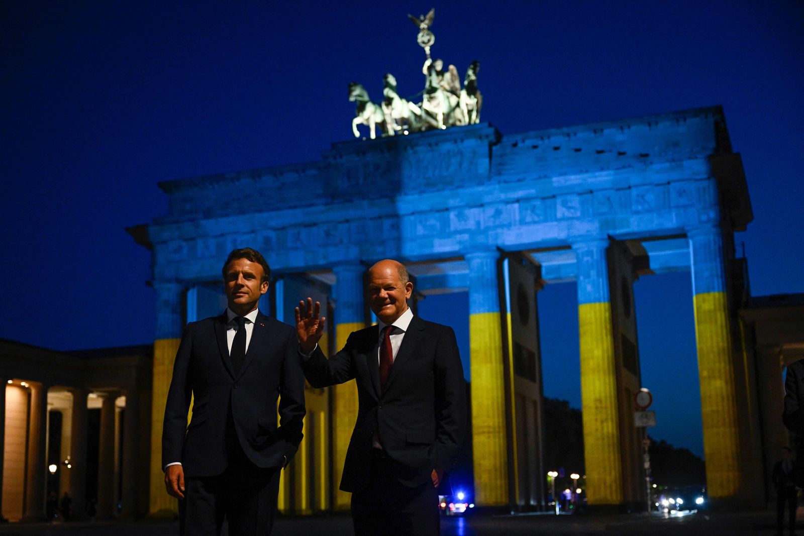 German Chancellor Olaf Scholz (R) and French President Emmanuel Macron visit the landmark Brandenburg Gate illuminated in the colors of the Ukrainian flag in Berlin on May 9, 2022, to show solidarity with Ukraine amid the ongoing Russian invasion. (Photo by John MACDOUGALL / AFP) - AFP