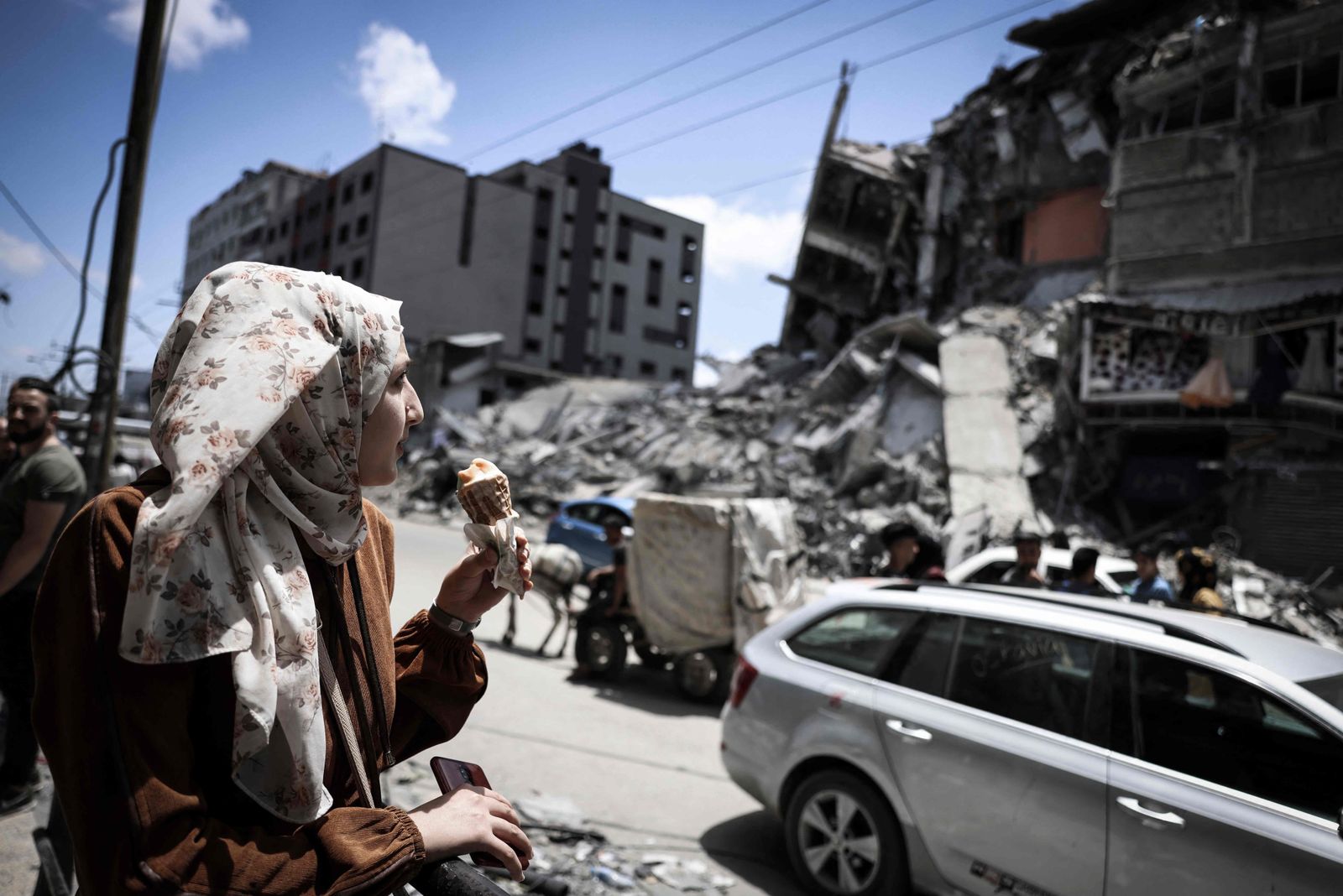 A Palestinian woman eats ice-cream in front of the destroyed Al-Shuruq building, destroyed by an Israeli air strike, on May 22, 2021, in Gaza City. - A ceasefire between Israel and Hamas, the Islamist movement which controls the Gaza Strip, appeared to hold today after 11 days of deadly fighting that pounded the Palestinian enclave and forced countless Israelis to seek shelter from rockets. (Photo by MAHMUD HAMS / AFP) - AFP