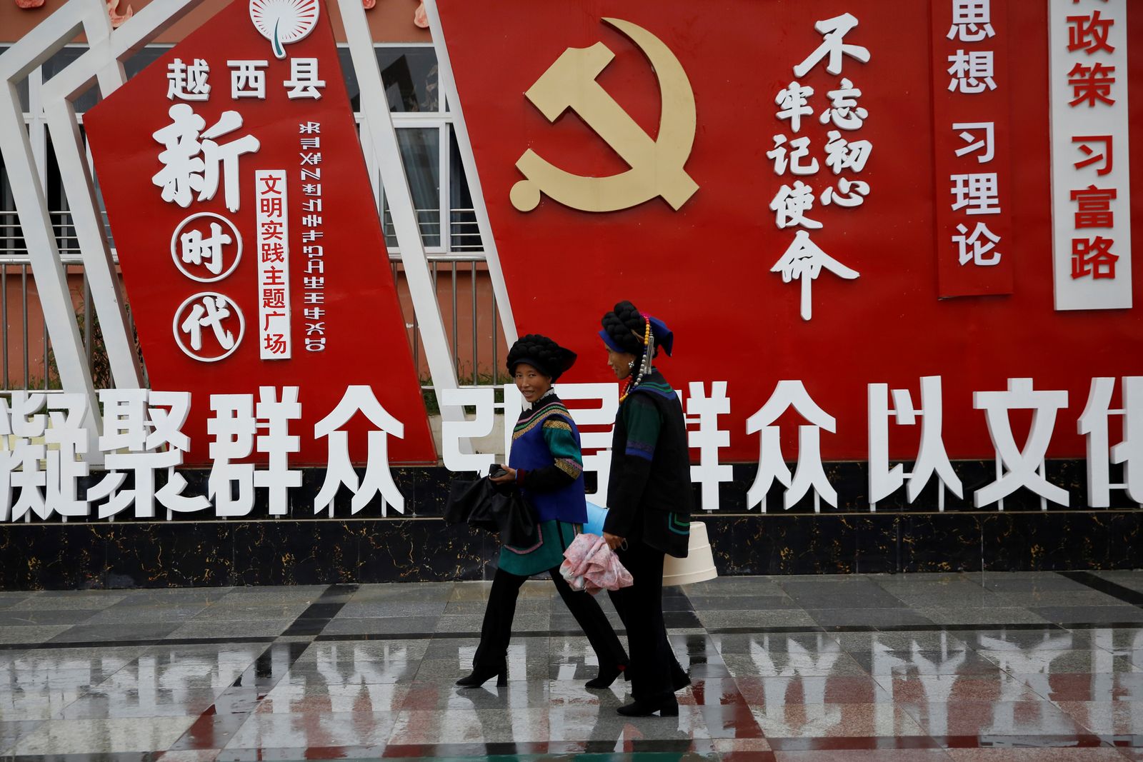 تسيران أمام شعار للحزب الشيوعي الصيني في مقاطعة سيشوان - 11 سبتمبر 2020 - REUTERS