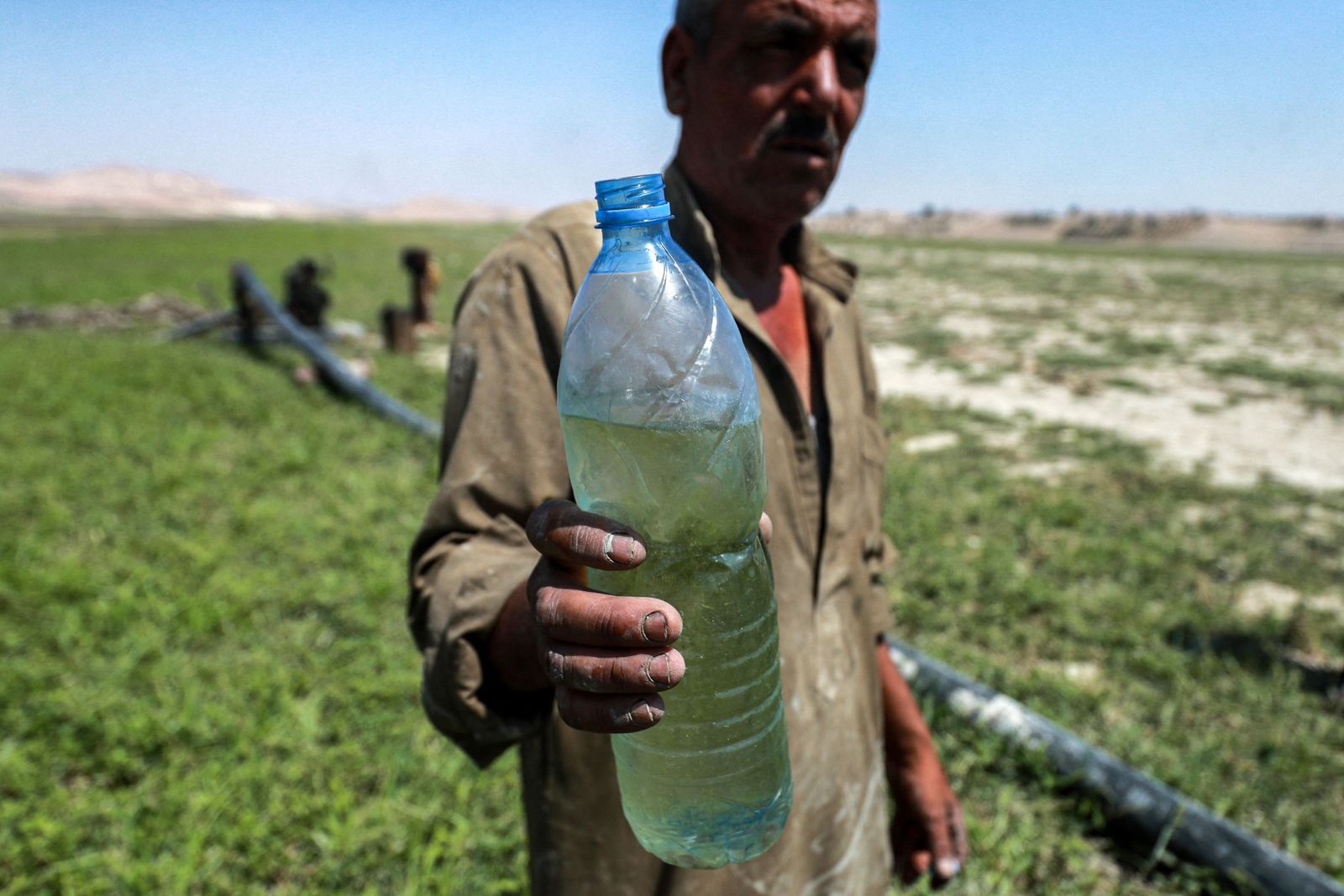 A man holds a nearly-full water bottle while standing near a pump drawing water from shallows of the Lake Assad reservoir along the Euphrates river by the town of Rumaylah in eastern Syria on July 25, 2021, as the area experiences unprecedented lower water levels since the dam was built in the mid-20th century. - Aid groups and engineers are warning of a looming humanitarian disaster in northeast Syria, where plummeting water levels at hydroelectric dams since January are threatening water and power cutoffs for millions amidst the coronavirus pandemic and economic crisis. Many in the Kurdish-held area are accusing neighbour and archfoe Turkey of weaponising water by tightening the tap upstream. (Photo by Delil SOULEIMAN / AFP) - AFP
